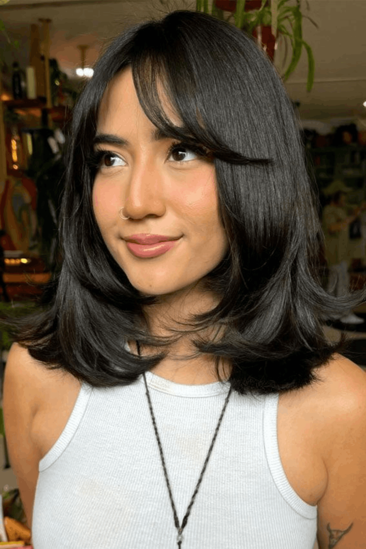 Woman with a short butterfly haircut, featuring soft layered ends and wispy bangs that lightly cover the forehead.