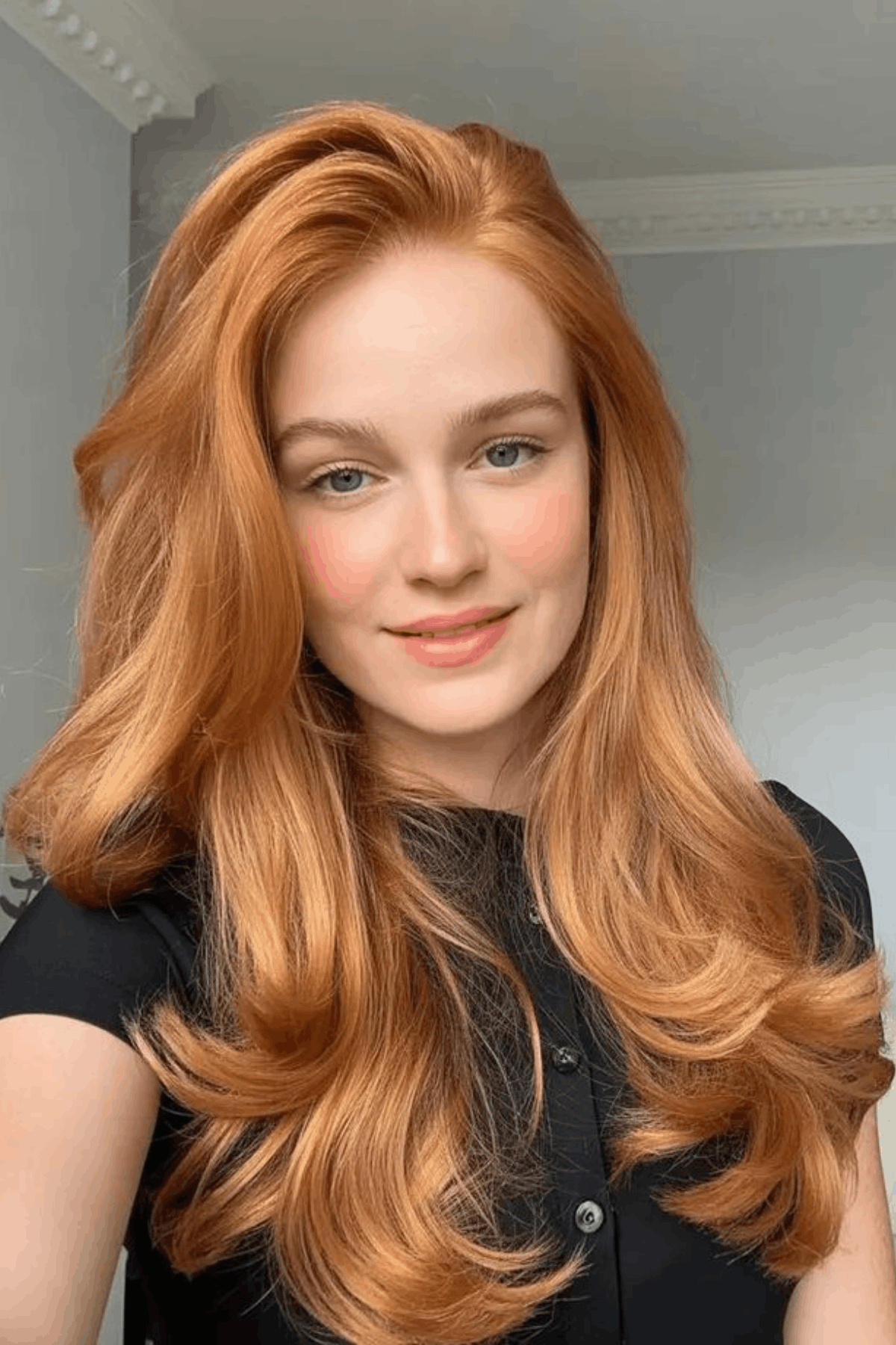 Woman with long strawberry copper orange hair, styled in soft, voluminous waves with a light, airy finish.