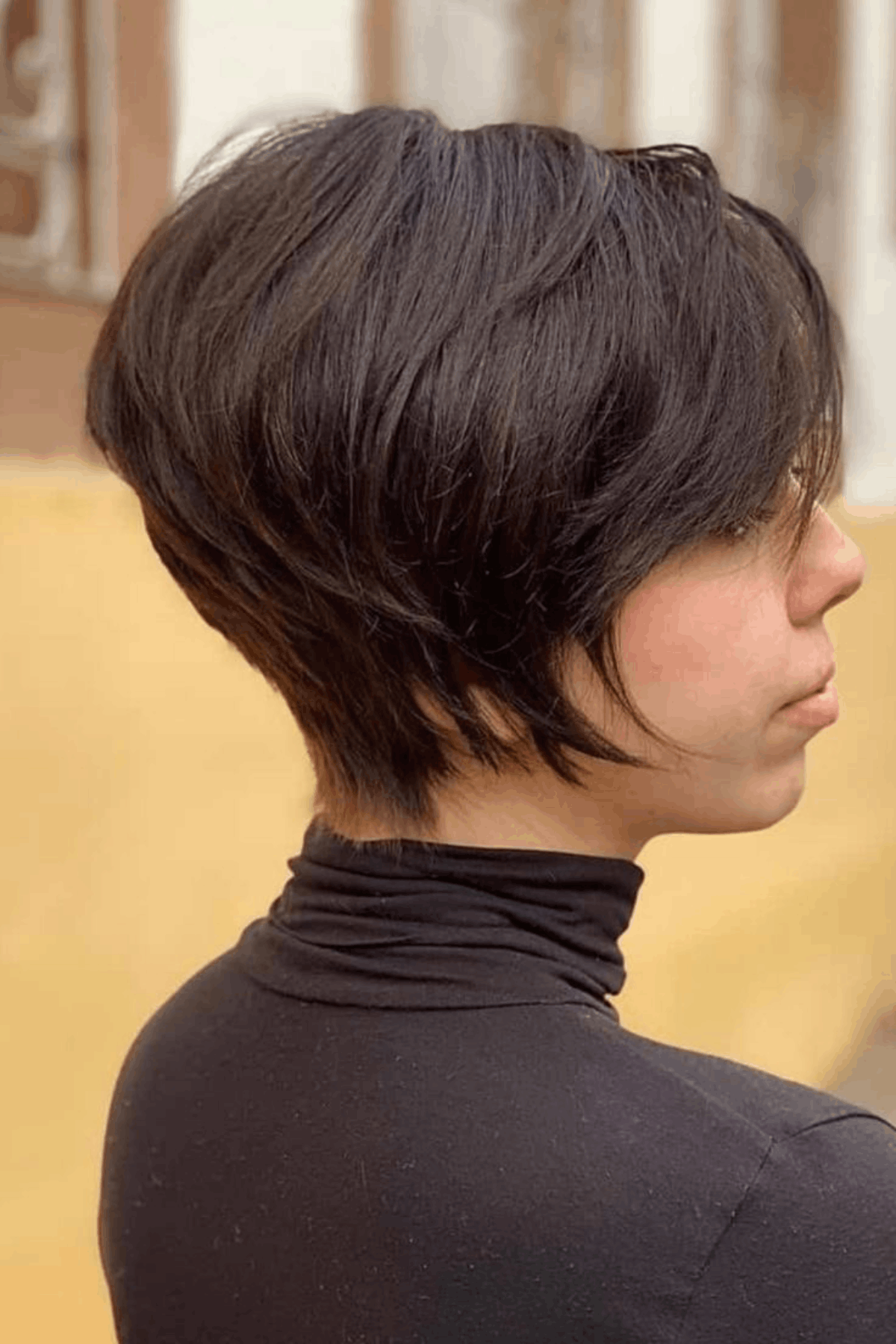 Side-profile image of a person wearing The Long Pixie with Tapered Neck, showing extended length on top and sides with a cleanly tapered neckline and soft, directional layers.