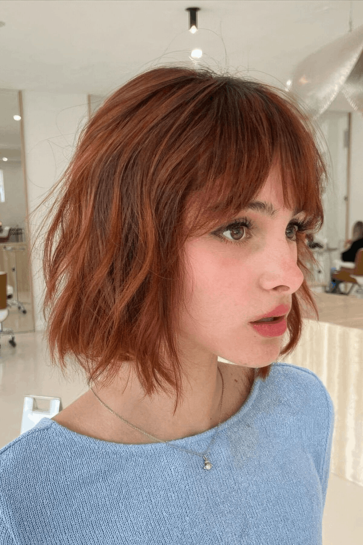 Side profile of a woman with a red choppy layered bob, featuring textured layers and slightly tousled ends.