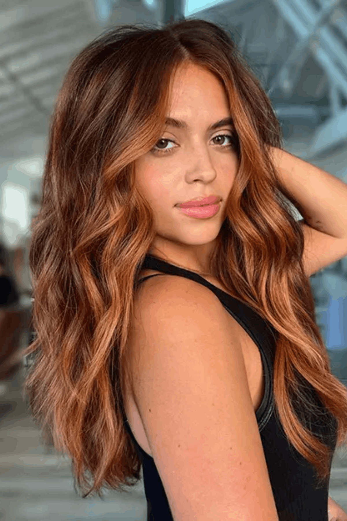 Portrait of a woman with wavy hair featuring orange balayage, blending warm copper tones into a natural base for a low-commitment color.