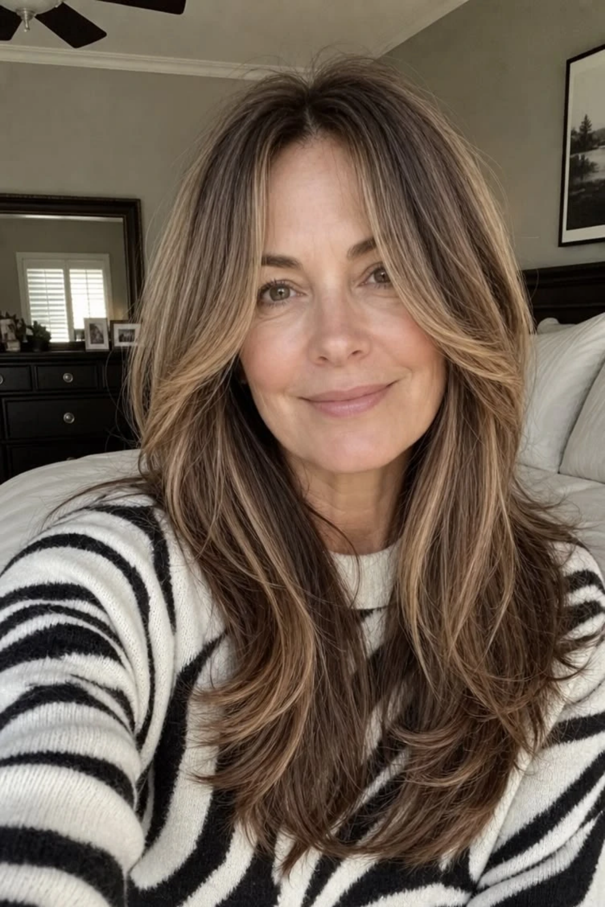 Long layers with curtain bangs on a woman in her fifties with brown and grey hair