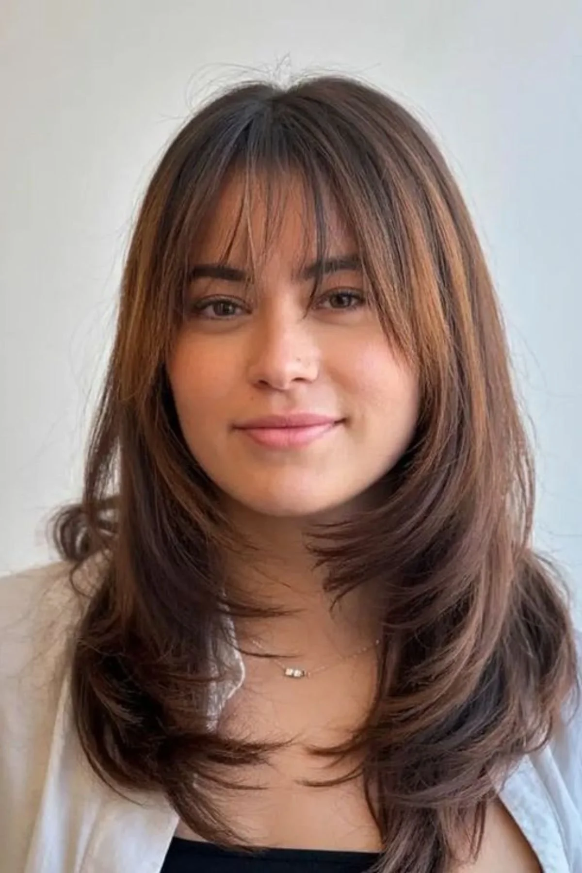 Woman styled in Wispy Bangs with Medium Layers haircut, featuring airy fringe and blended layers for soft texture.