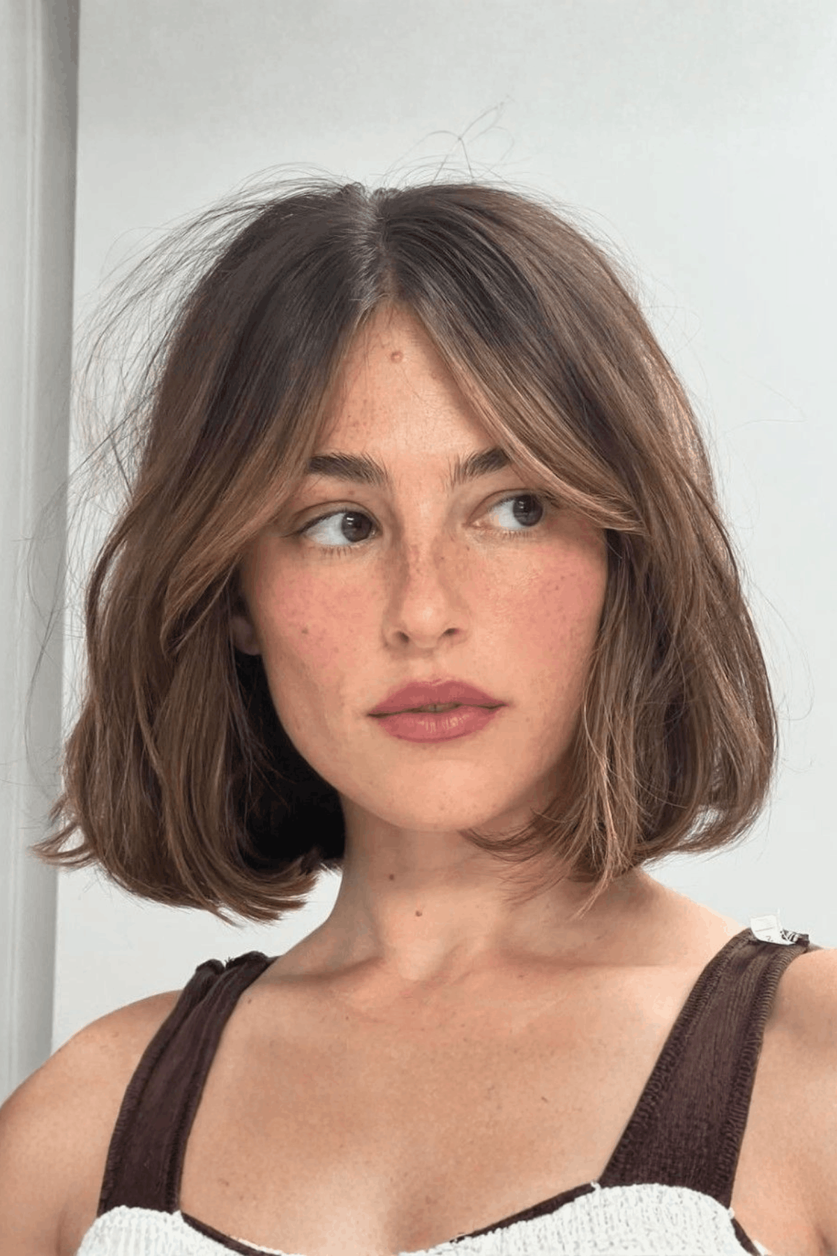 Portrait of a woman with a brown soft layered bob with curtain fringe, styled with gentle layers and parted face-framing bangs.