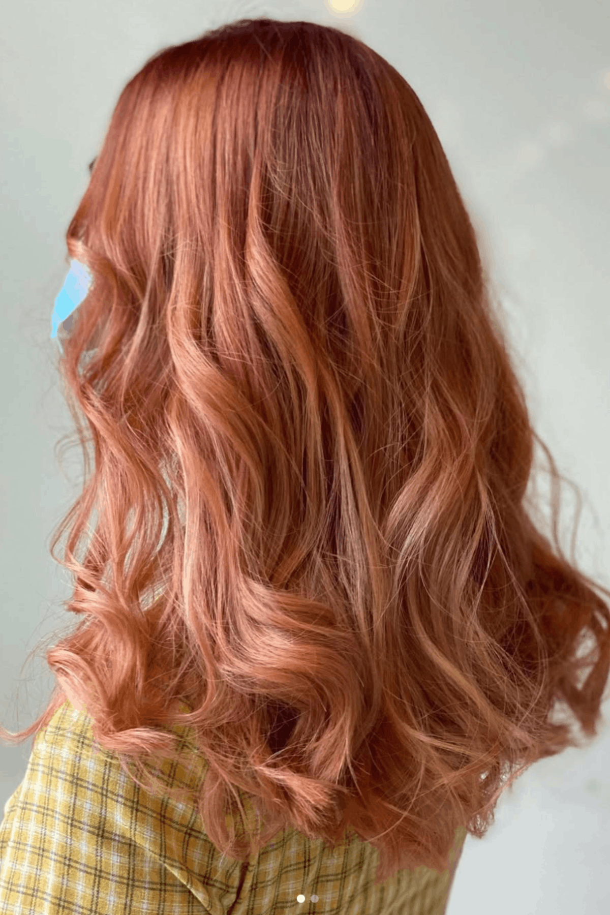 Back view of a woman with wavy rose gold and orange blended hair, creating a soft, trendy warm-toned look.