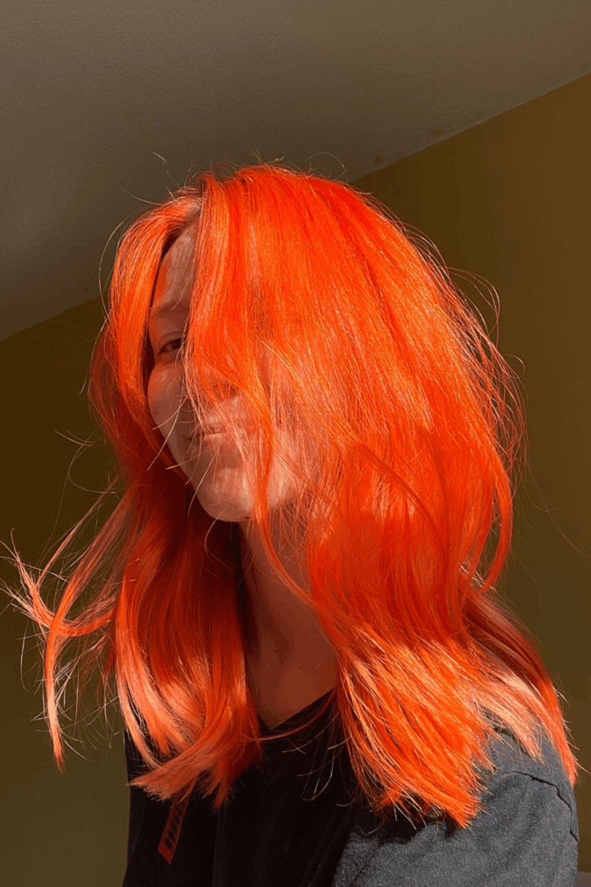 Portrait of a woman with vivid neon orange hair, styled in loose layers with high-shine, bold statement color.