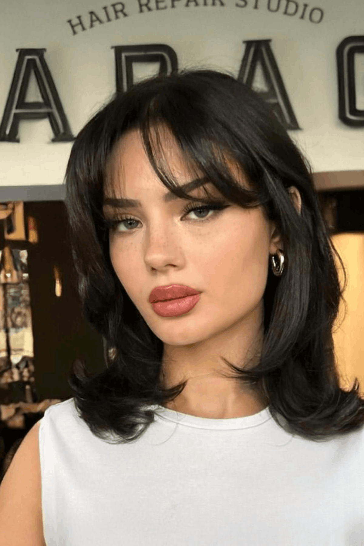 Woman with a short butterfly haircut, featuring layered volume and curtain bangs parted at the center, softly framing the face.