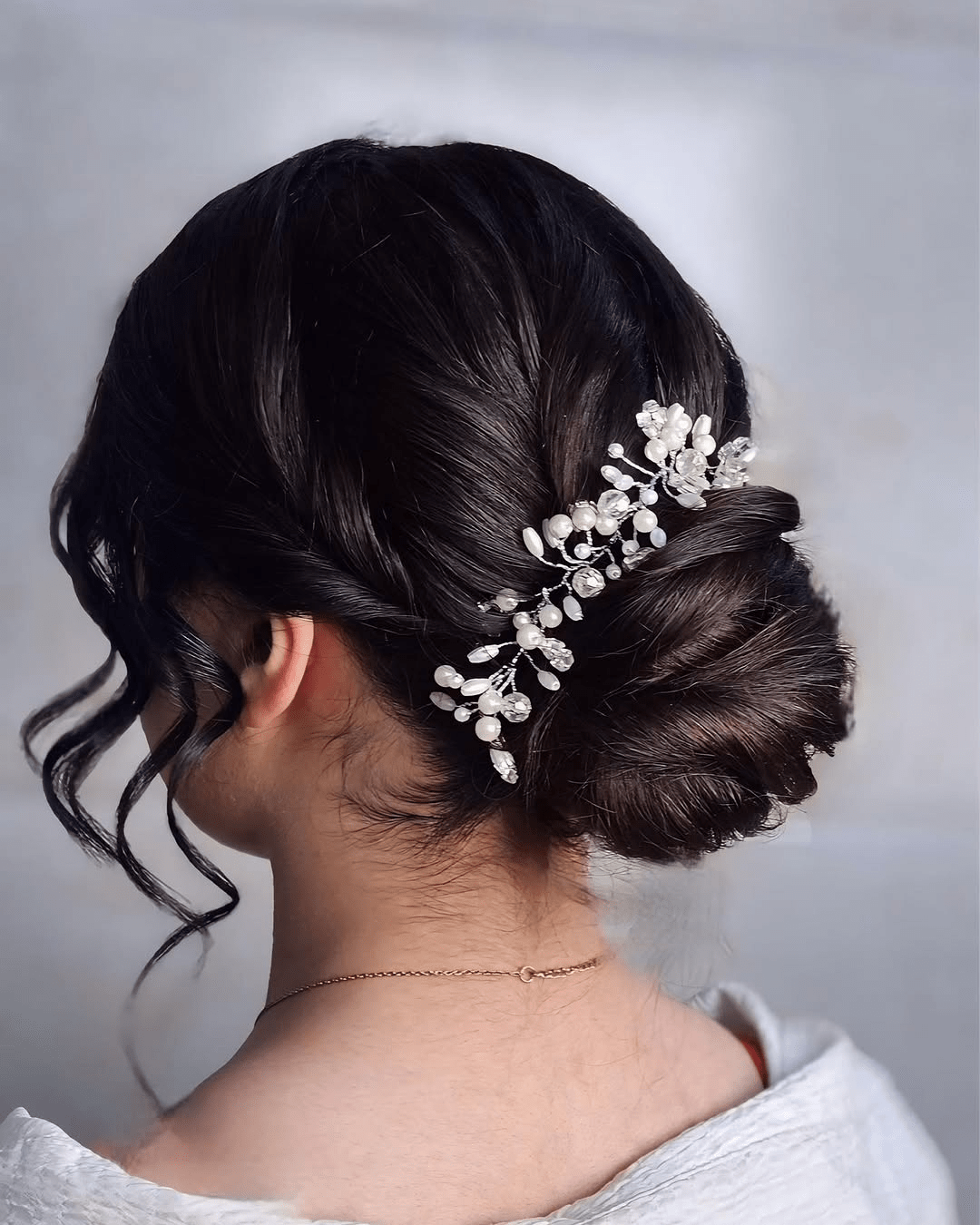 Twisted Low Chignon with Bobby-Pin Texture hairstyle featuring smooth dark hair styled into a low bun, accented with delicate pearl and crystal hairpin, and soft face-framing curls.