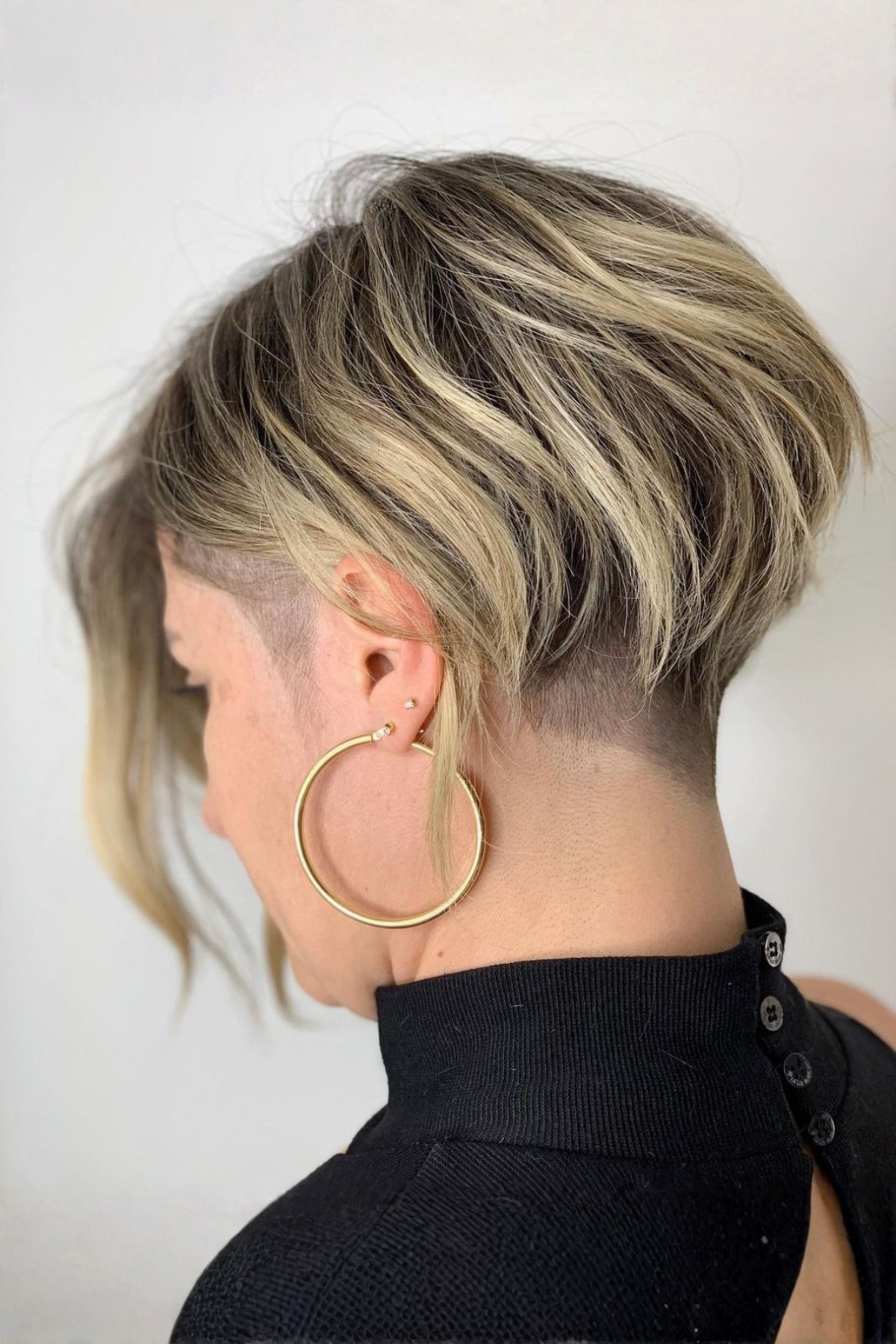 Back and side view of a person wearing Long Pixie with Undercut Accent, showcasing longer textured layers on top contrasted with a closely cropped undercut around the sides and nape.