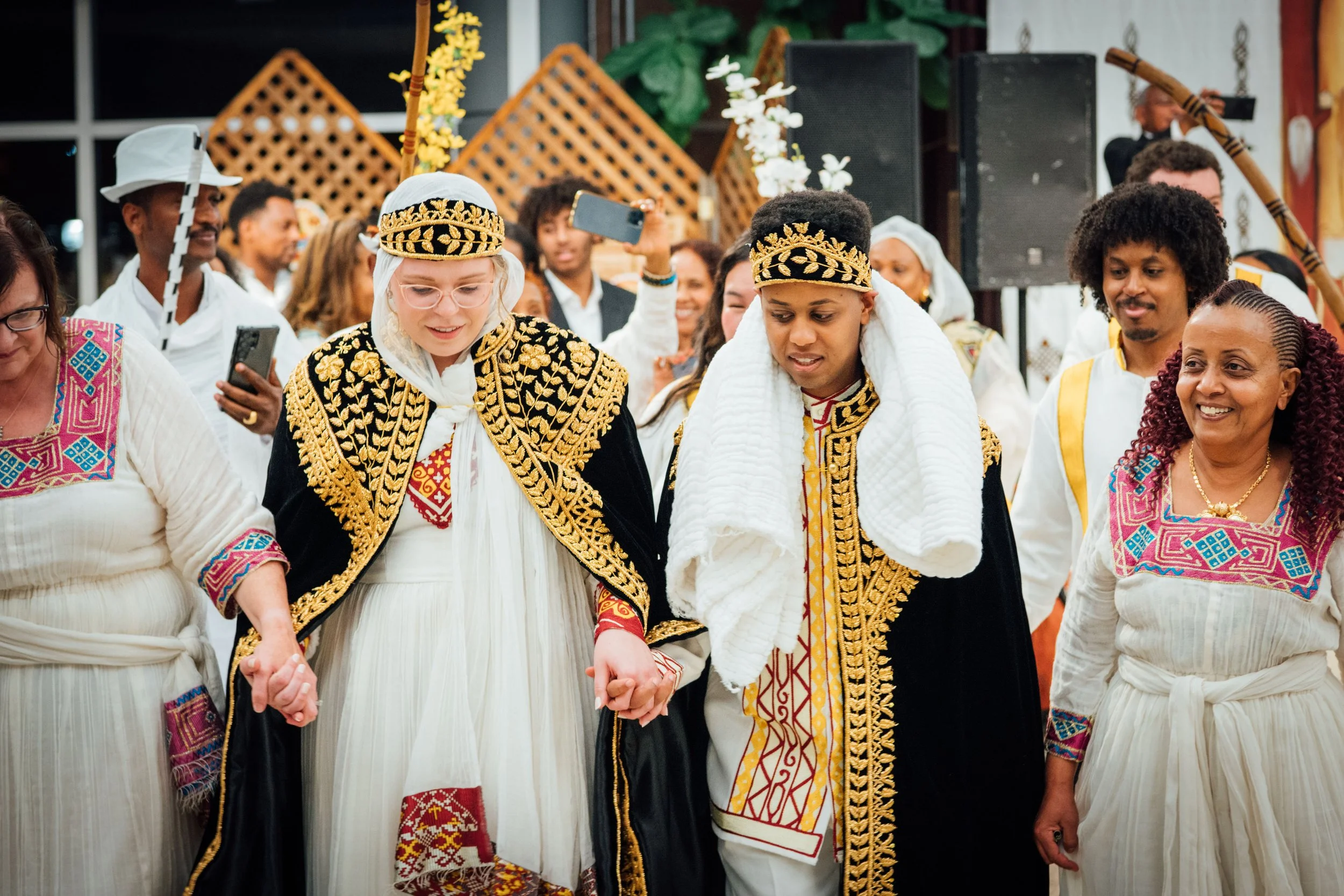 Group of people dressed in traditional African clothing, holding hands in a circle, participating in a cultural event or celebration.
