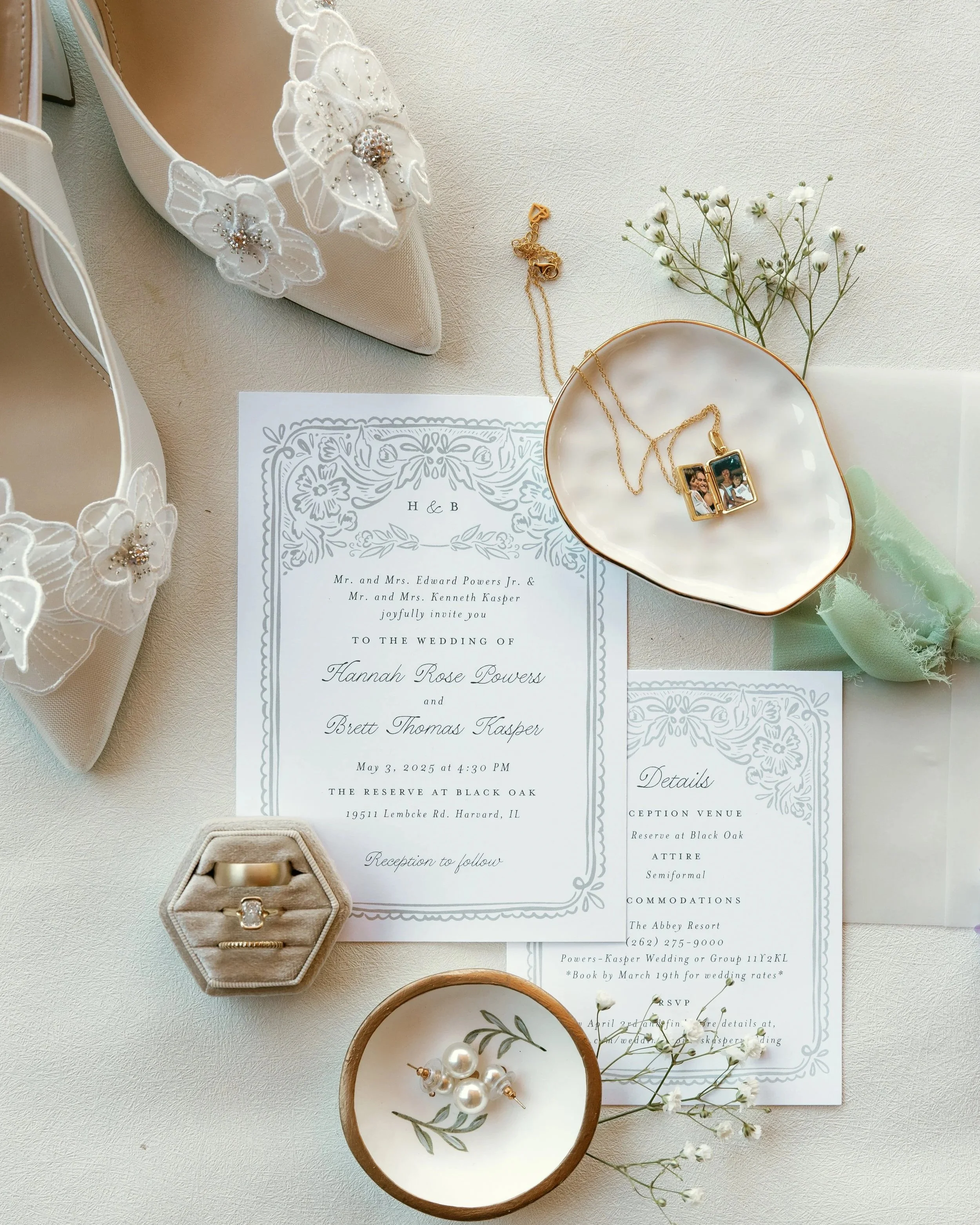 Invitation card for a wedding with floral designs, gold jewelry including a necklace and a photo pendant, white flower petals, pearl earrings, a small white bowl with pearl jewelry, and a beige shoe with floral embroidery.
