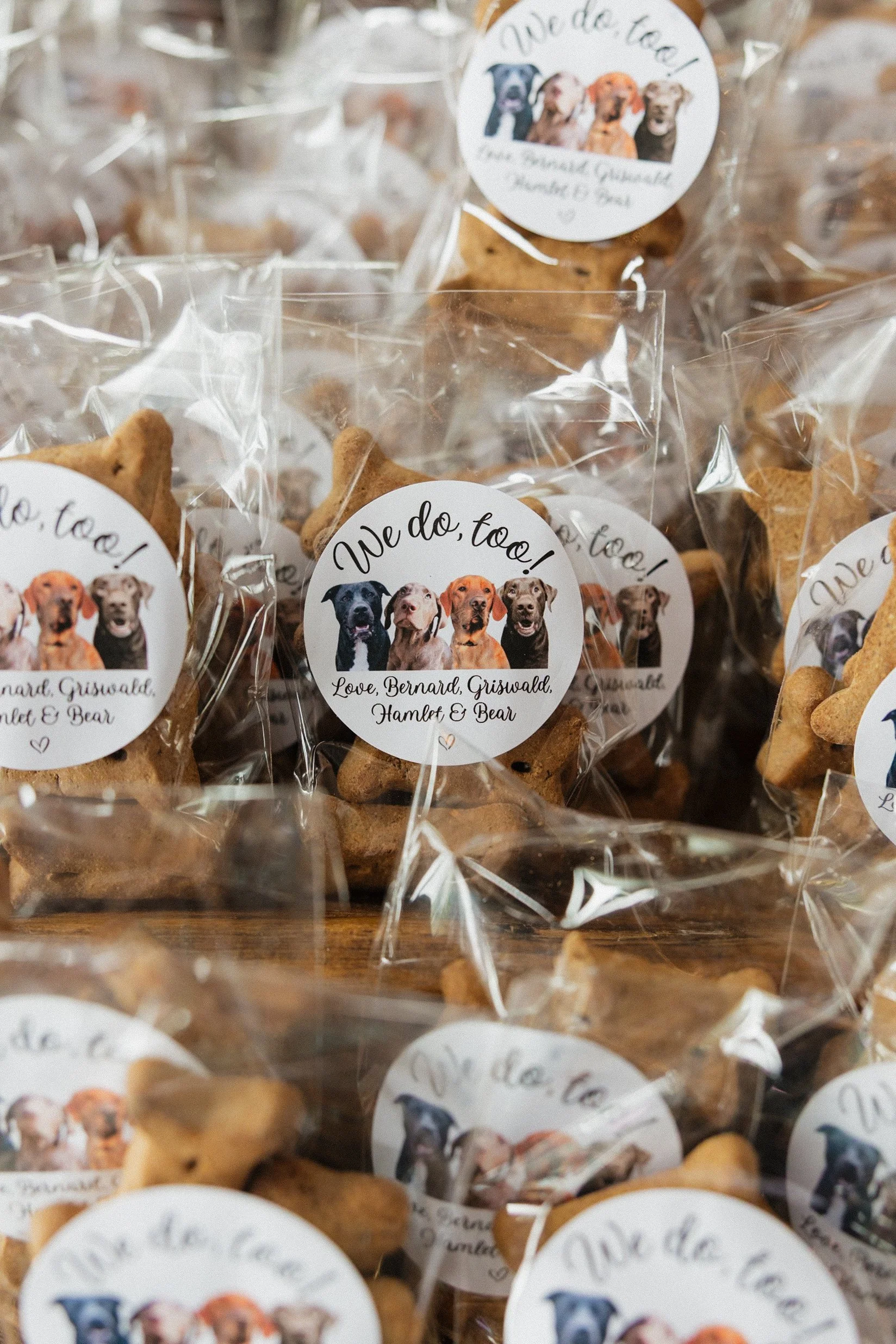 Assorted dog-shaped cookies wrapped in clear plastic, with a label that says "We do, too! Love, Bernard, Griswald, Hamlet, & Bear," featuring illustrations of four different dogs.