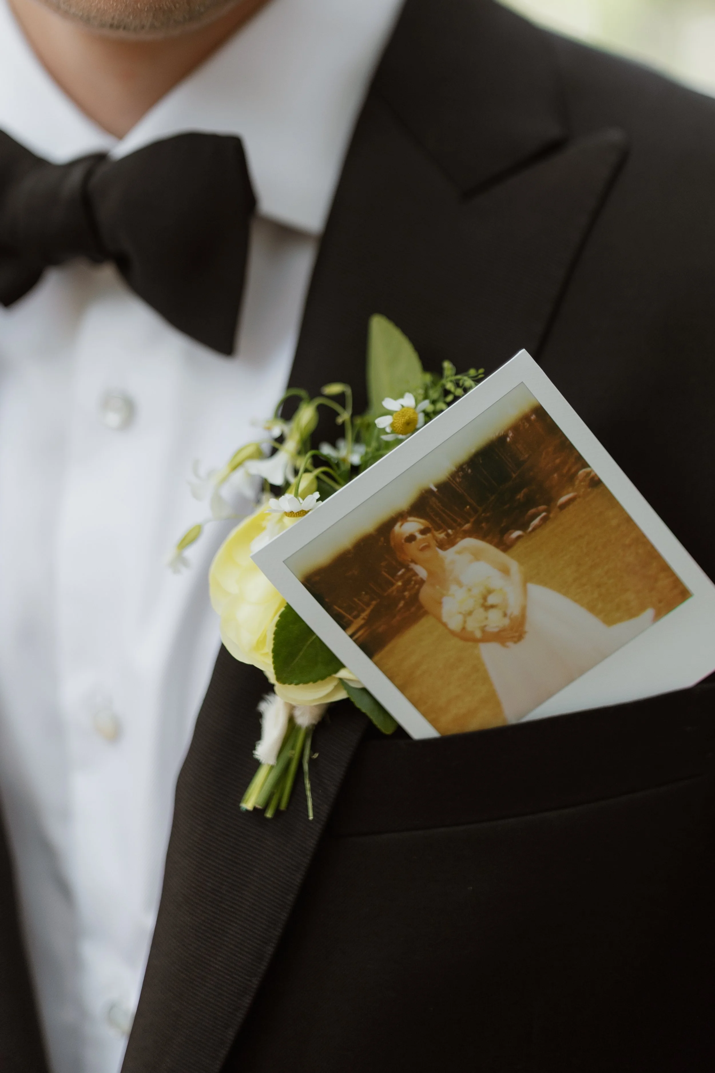 Close-up of a person in a tuxedo holding a wedding or event photograph, with floral accents attached to the attire.
