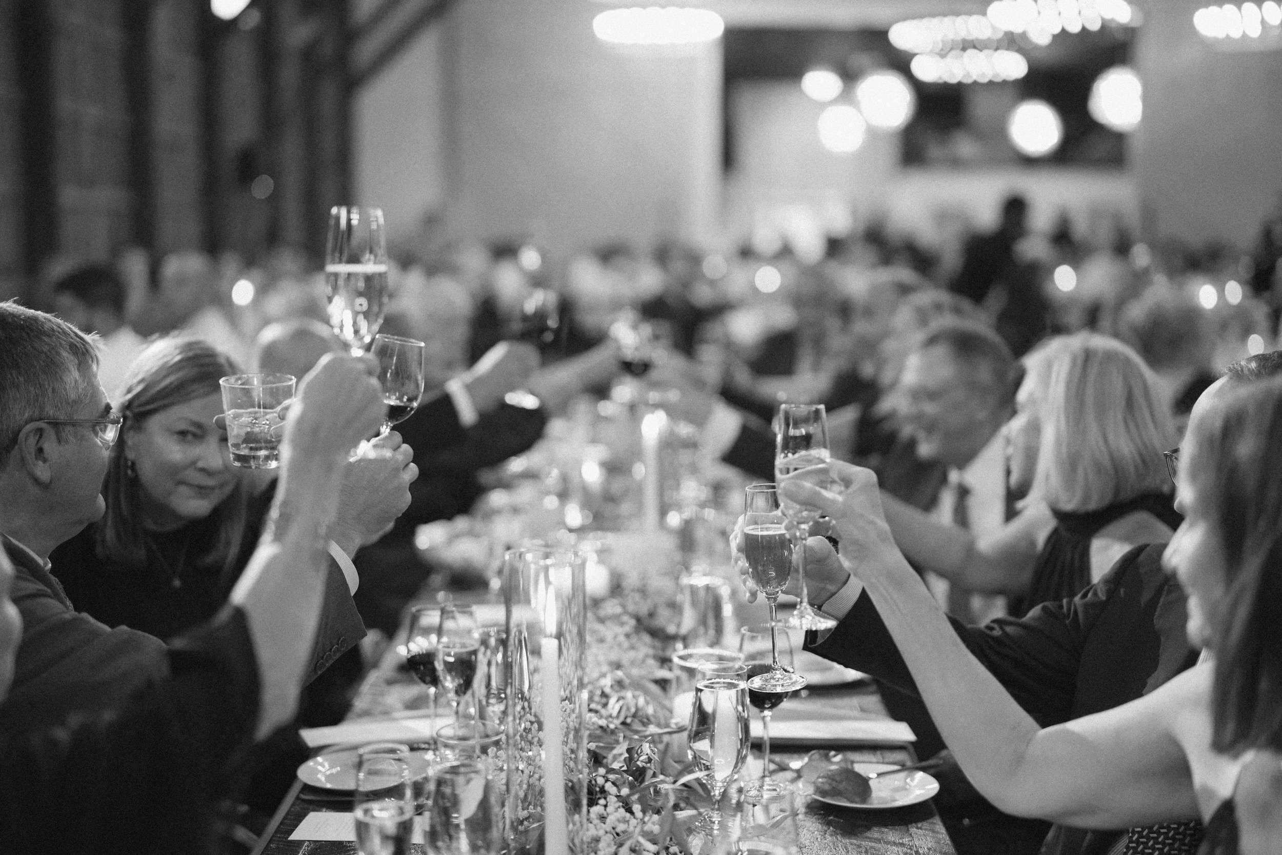 People sitting at a long table raising glasses in a toast during a formal dinner event.