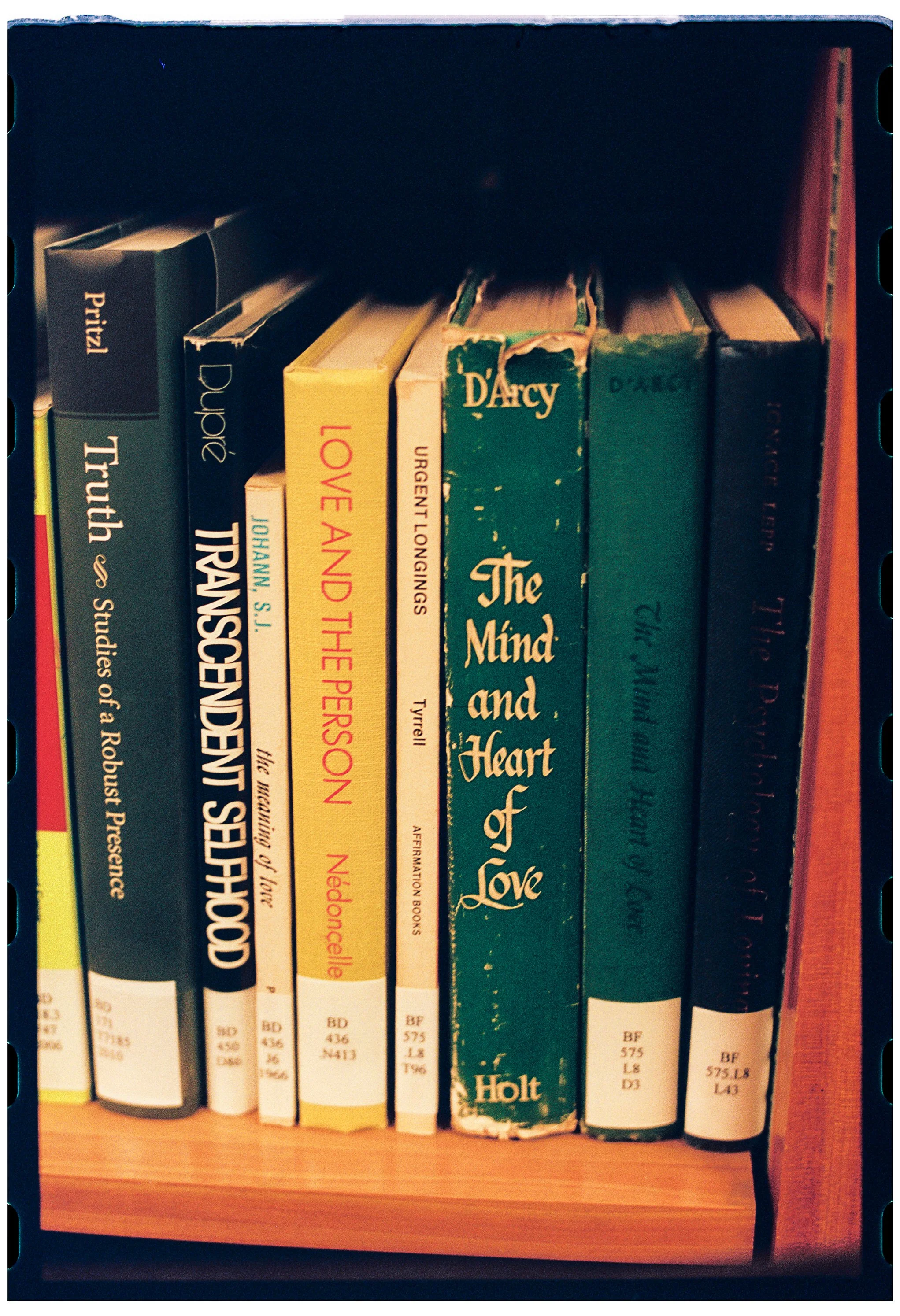 A bookshelf with various books, some worn, with visible titles including "The Mind and Heart of Love" and "Travels of a Robusta."