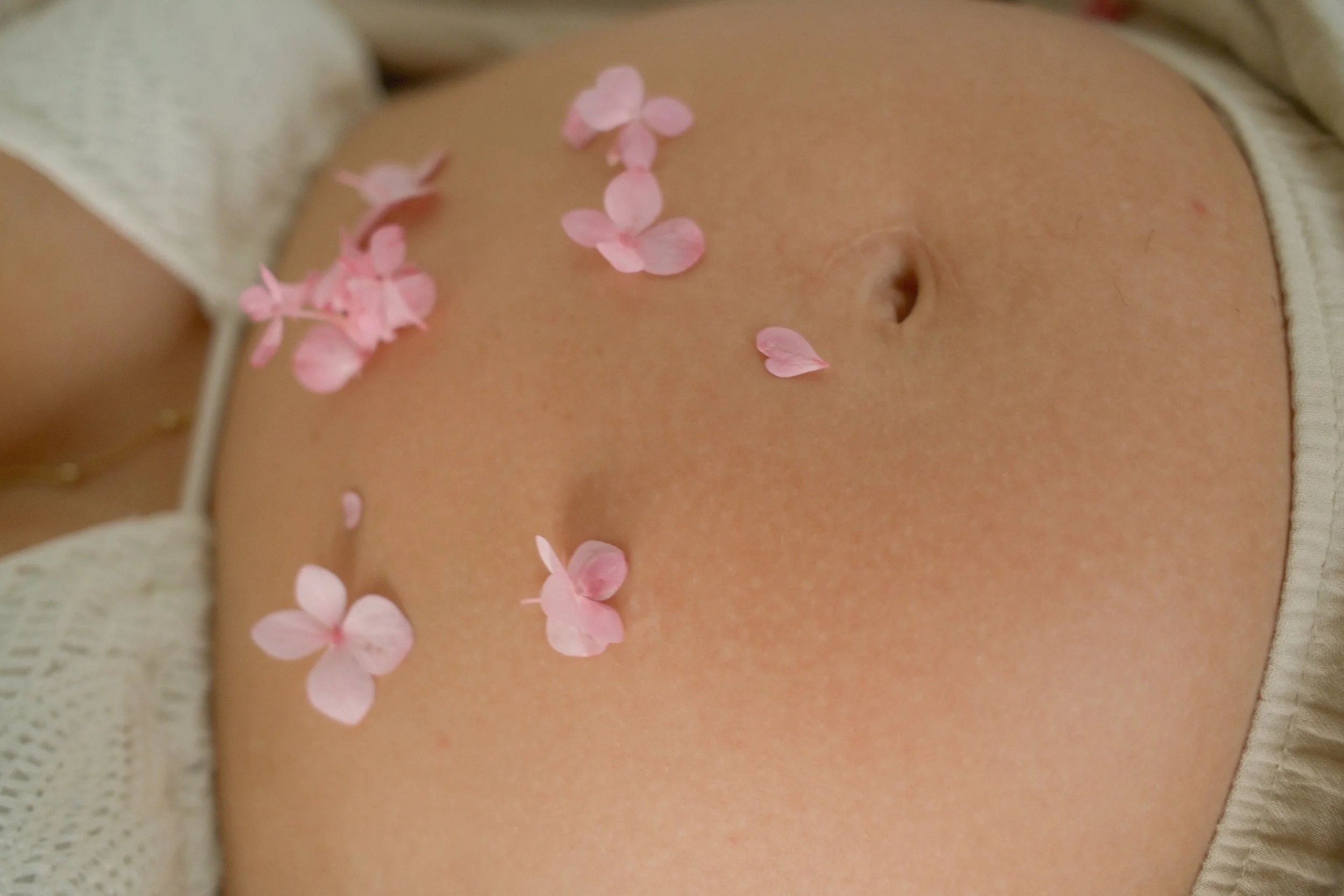 Close-up of a person's abdomen with pink flower petals scattered on the skin.
