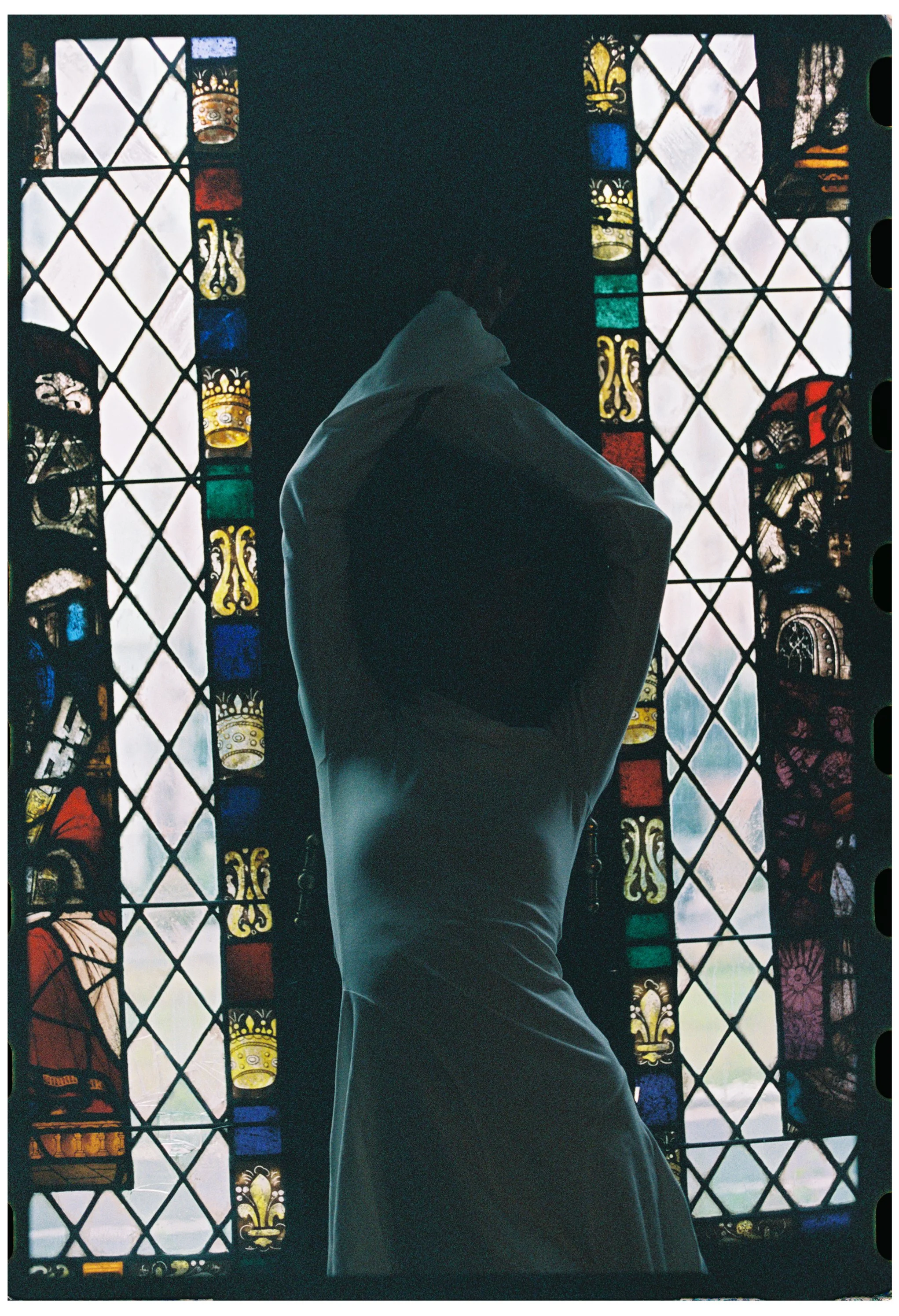 Person standing inside a church or cathedral, facing stained glass windows depicting religious or historical scenes, with only the back of their head and shoulders visible.