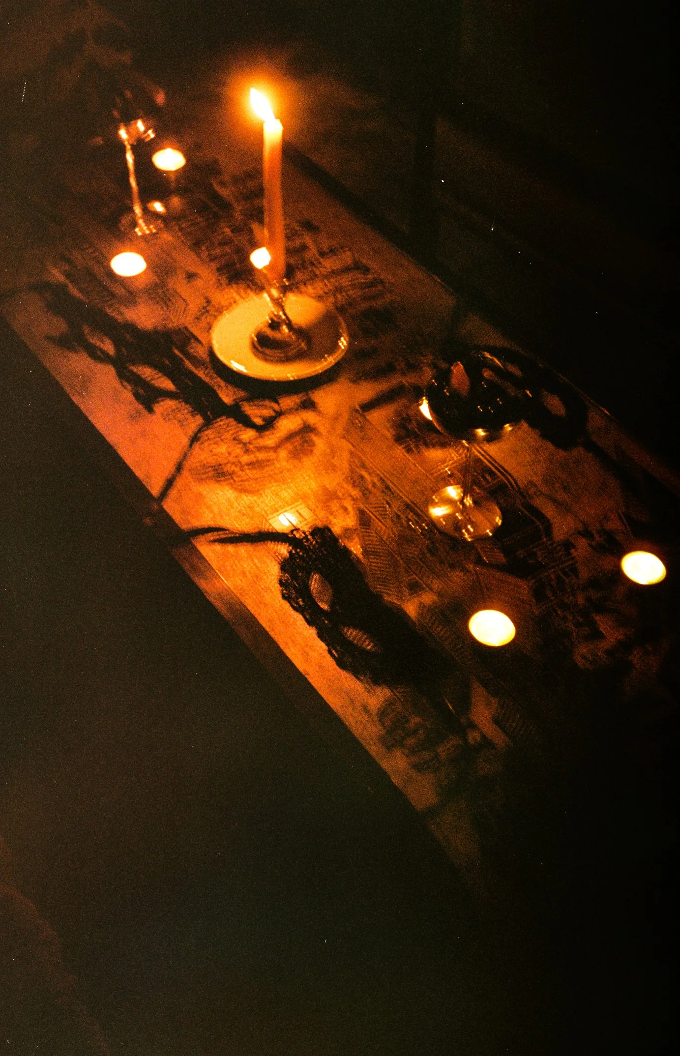 A dark scene with a table setting that includes a candle, a glass of wine, and casual items, cast in warm, dim lighting.