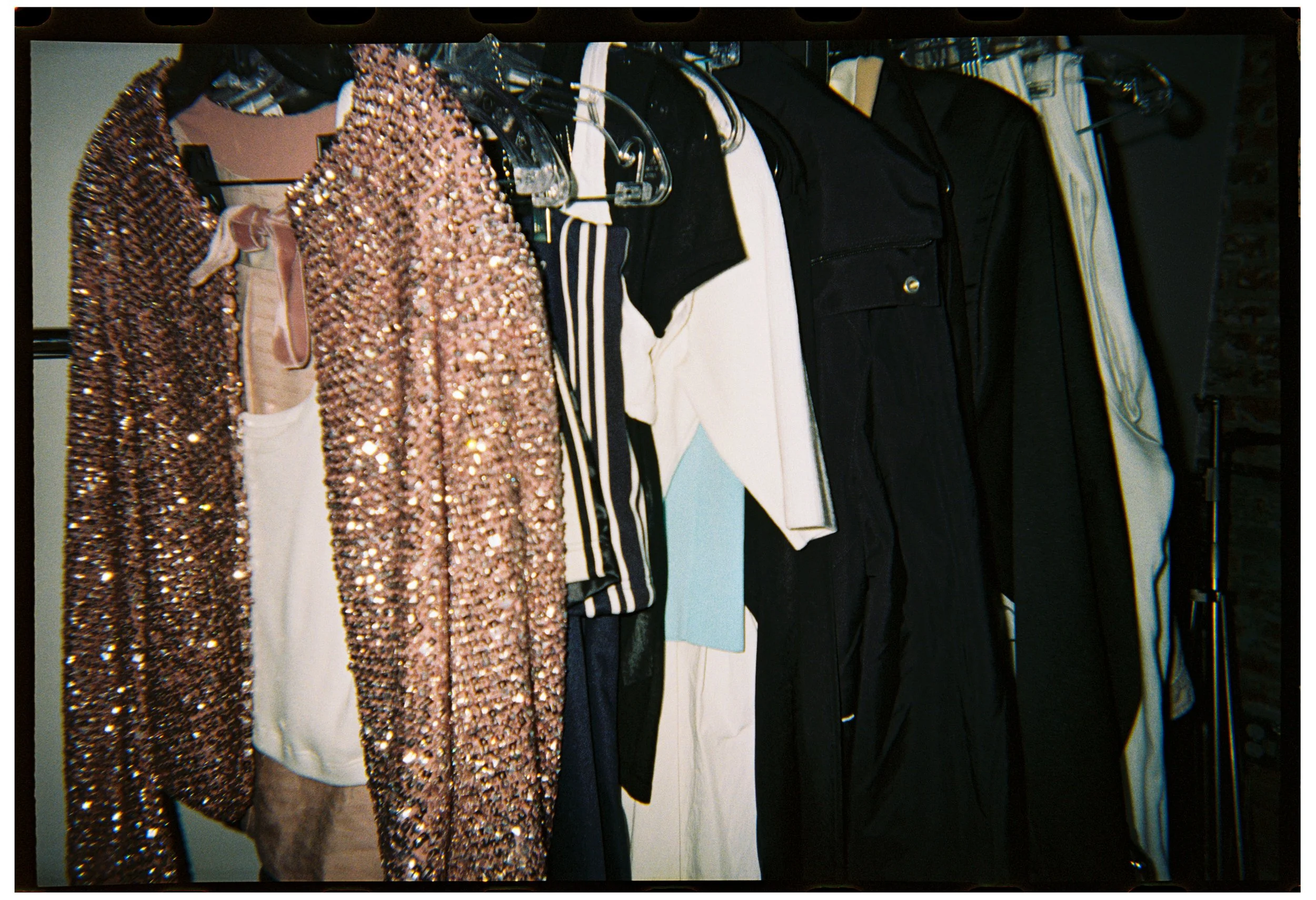 Clothes on a rack, including a sequined pink jacket, black pants, striped shirt, and other garments.