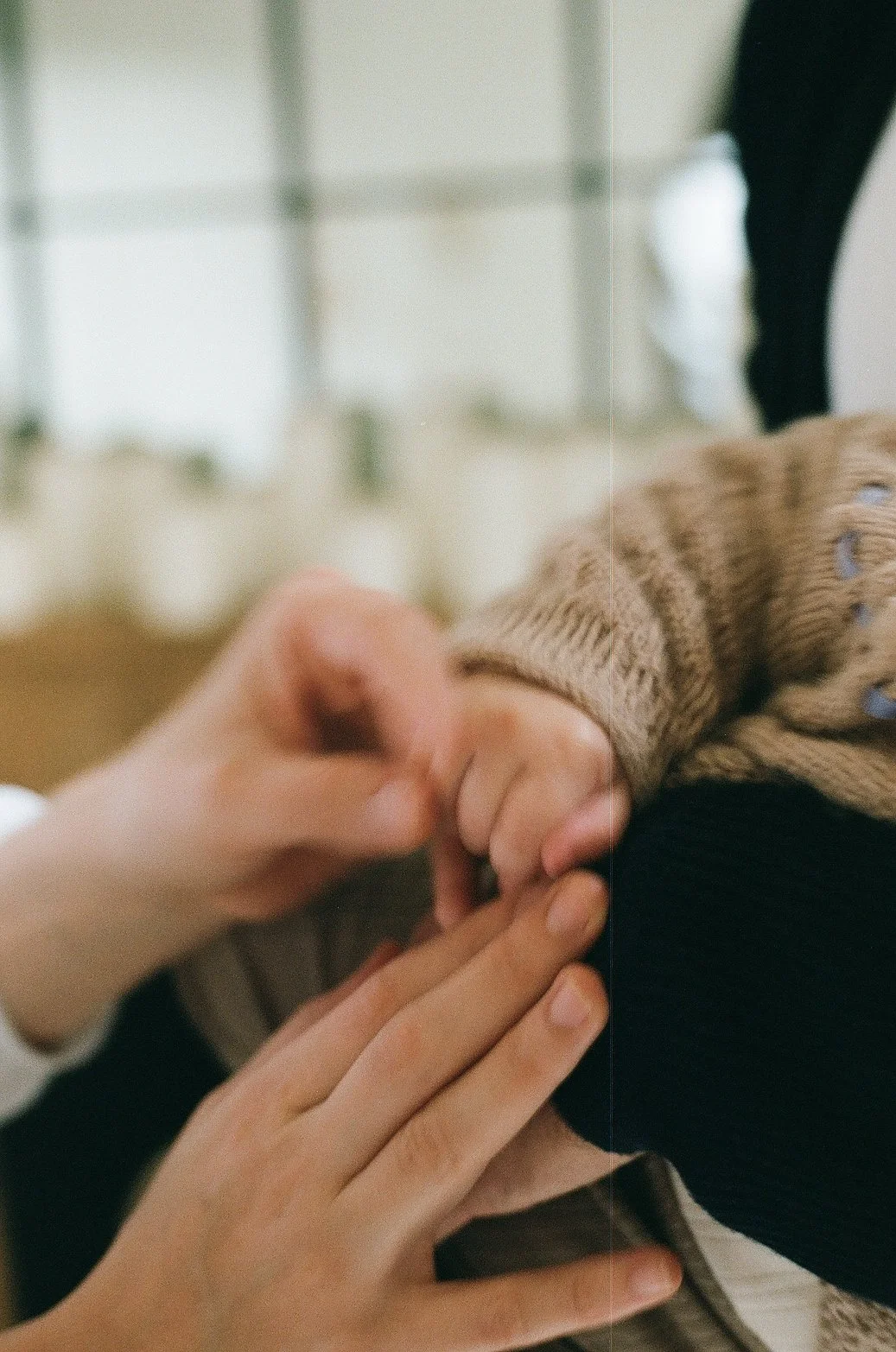 Close-up of a person's hand holding a child's hand, with a blurred background.