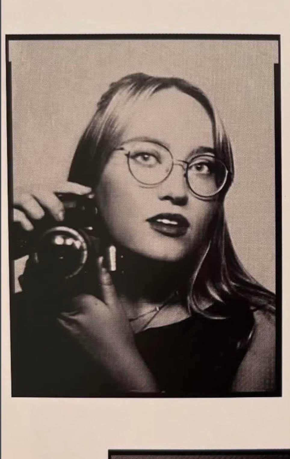 Black and white portrait of a woman with glasses holding a vintage rotary phone to her ear.