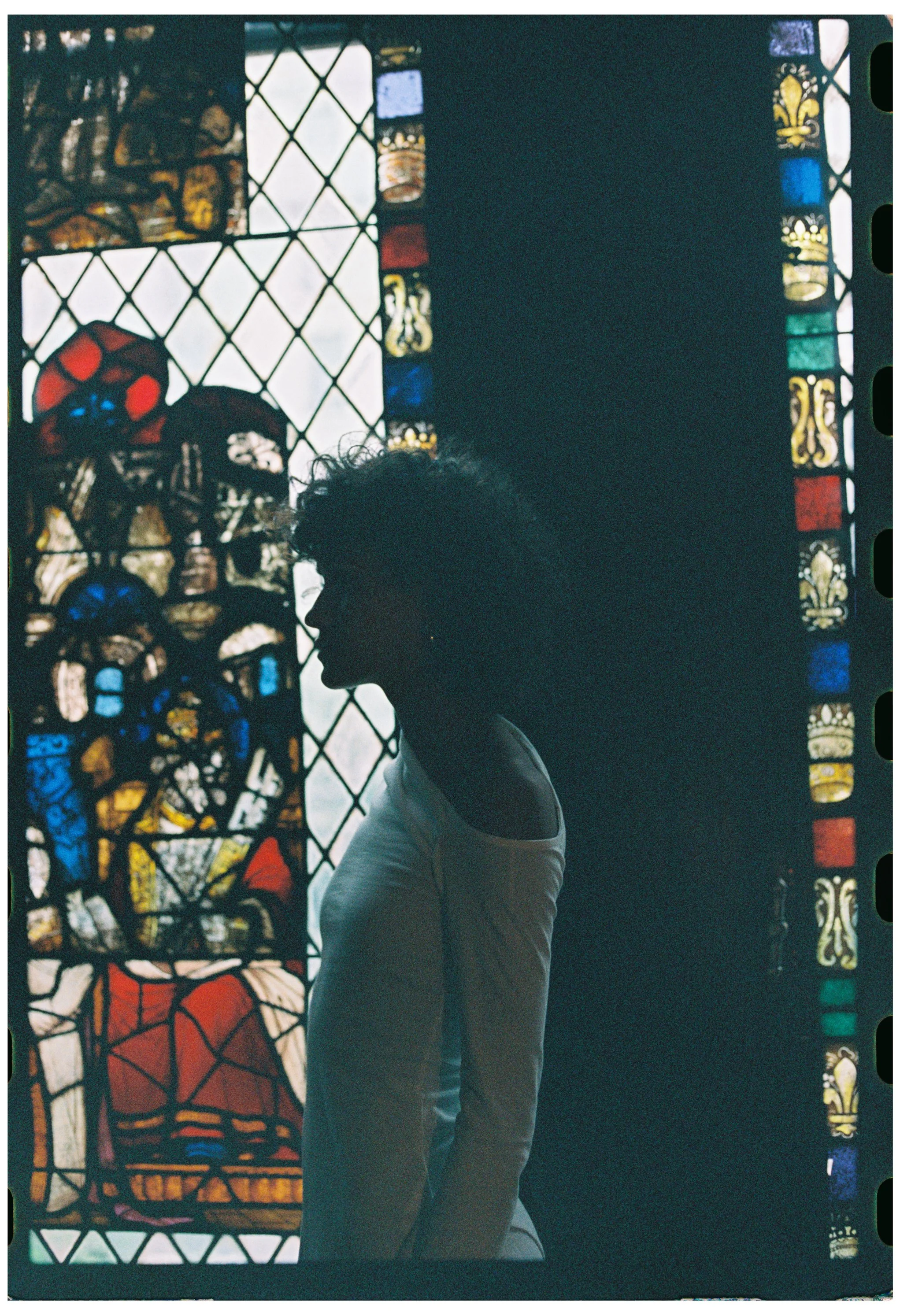 Silhouette of a person in front of a stained glass window with vibrant colors and intricate designs, backlit by bright light.