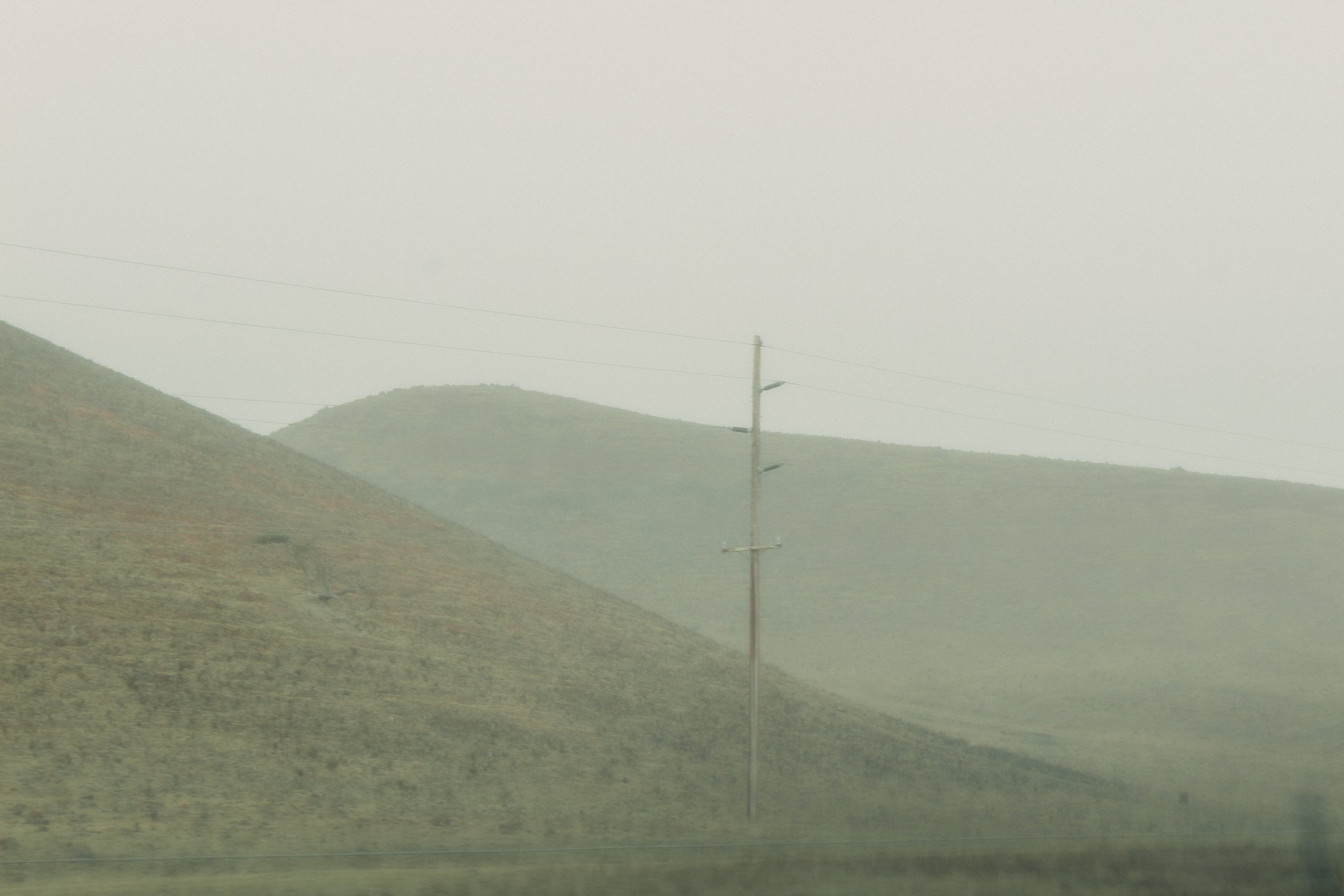 Hazy landscape with rolling hills and an electric utility pole against a foggy sky.