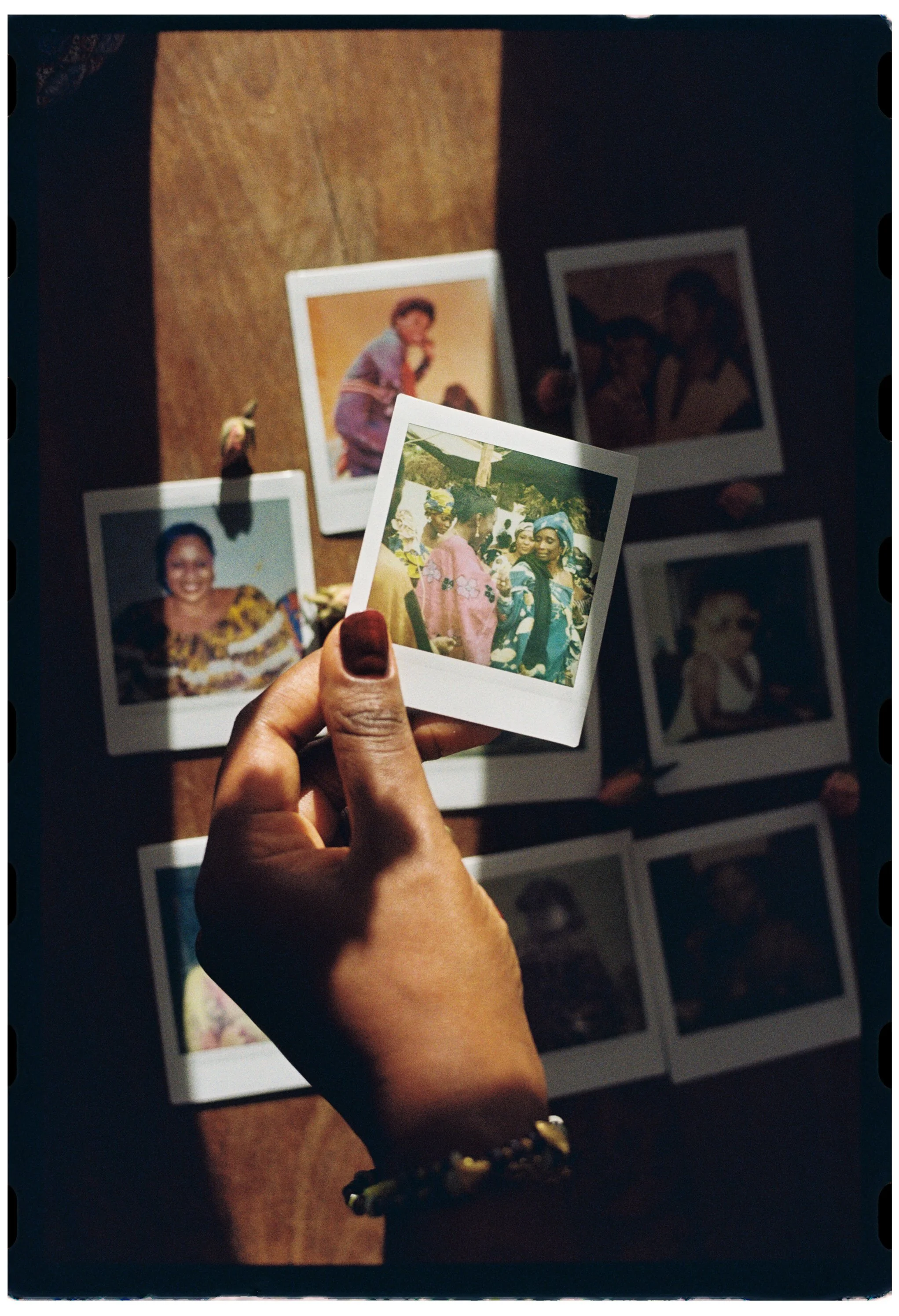 A person holding a group of printed photographs or Polaroids, with several photos laid out on a wooden surface in the background.