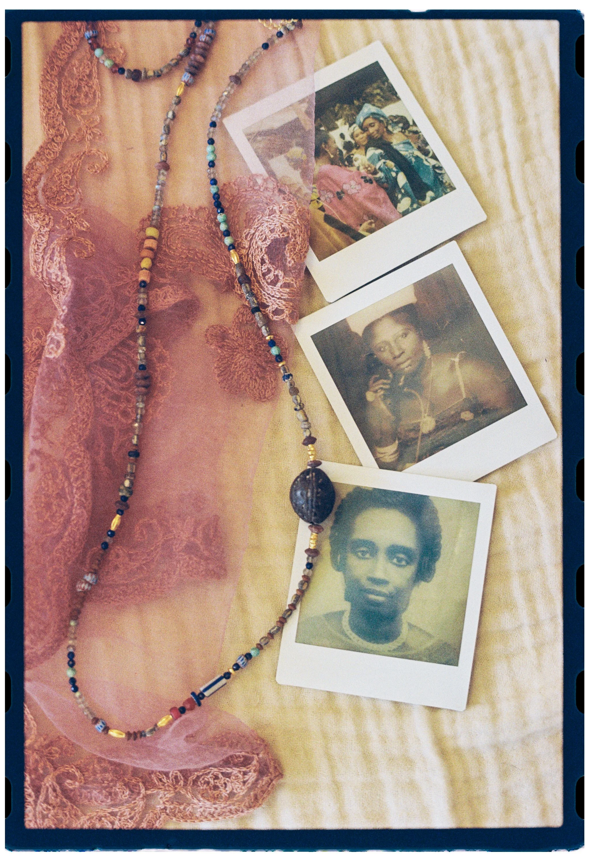 Colorful beaded necklace, vintage photographs of women, lace fabric, and a yellow cloth background.