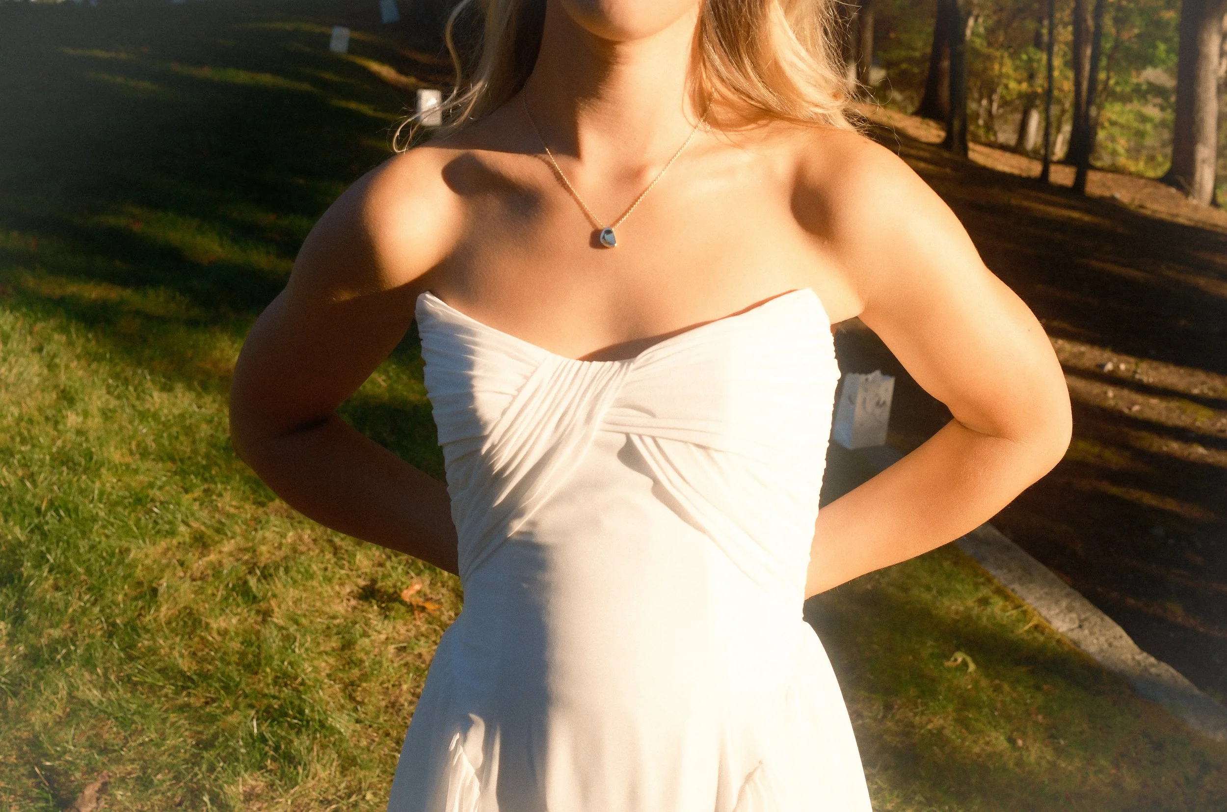 A bride in a white strapless wedding dress, standing outdoors at golden hour in golden light. Shot on 35mm film at an east coast backyard wedding