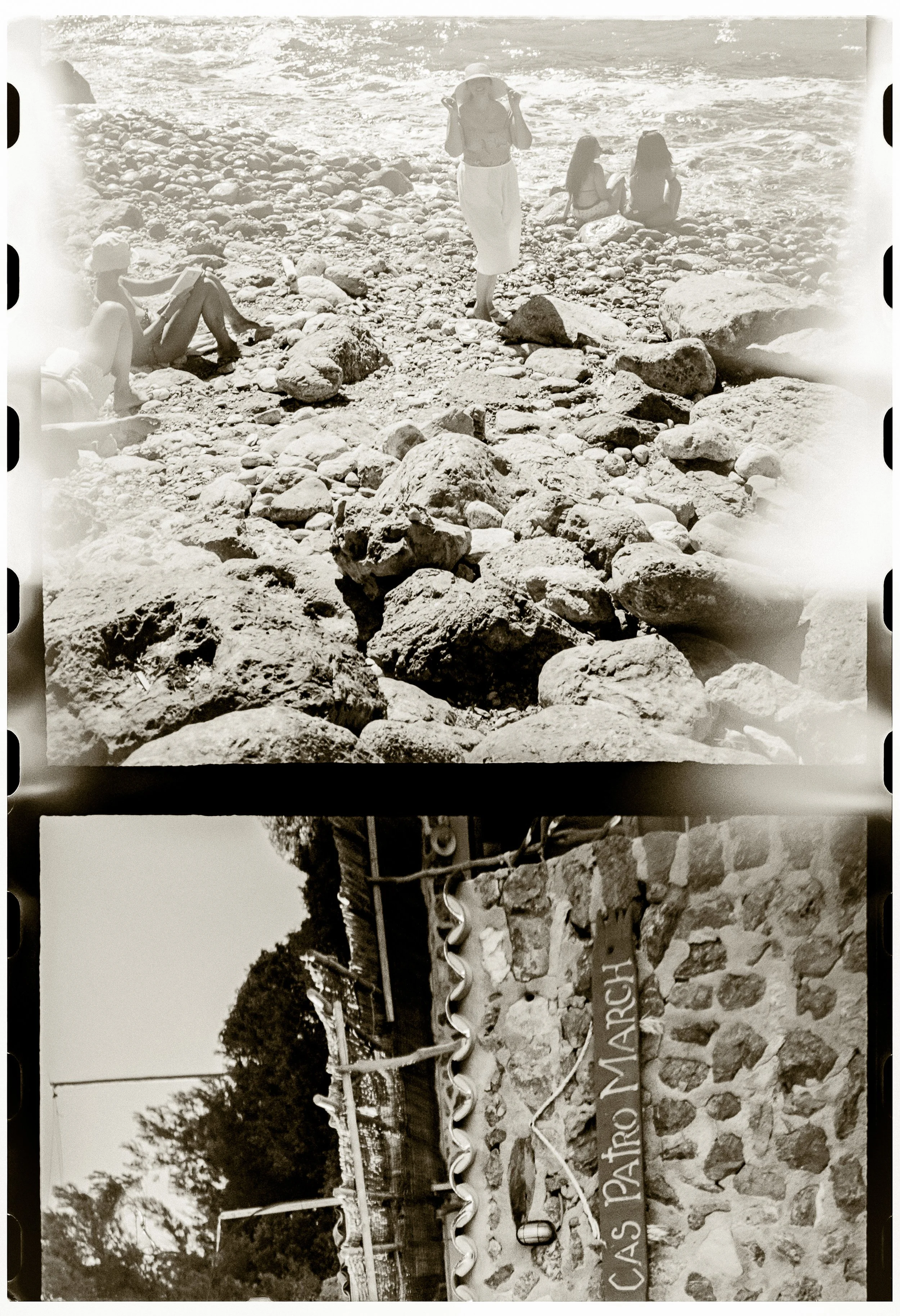 A black and white photo of a rocky beach with a woman walking and two women sitting by the water. Sign reads "CASA MARO 310". mallorca destination wedding Shot on 35mm film