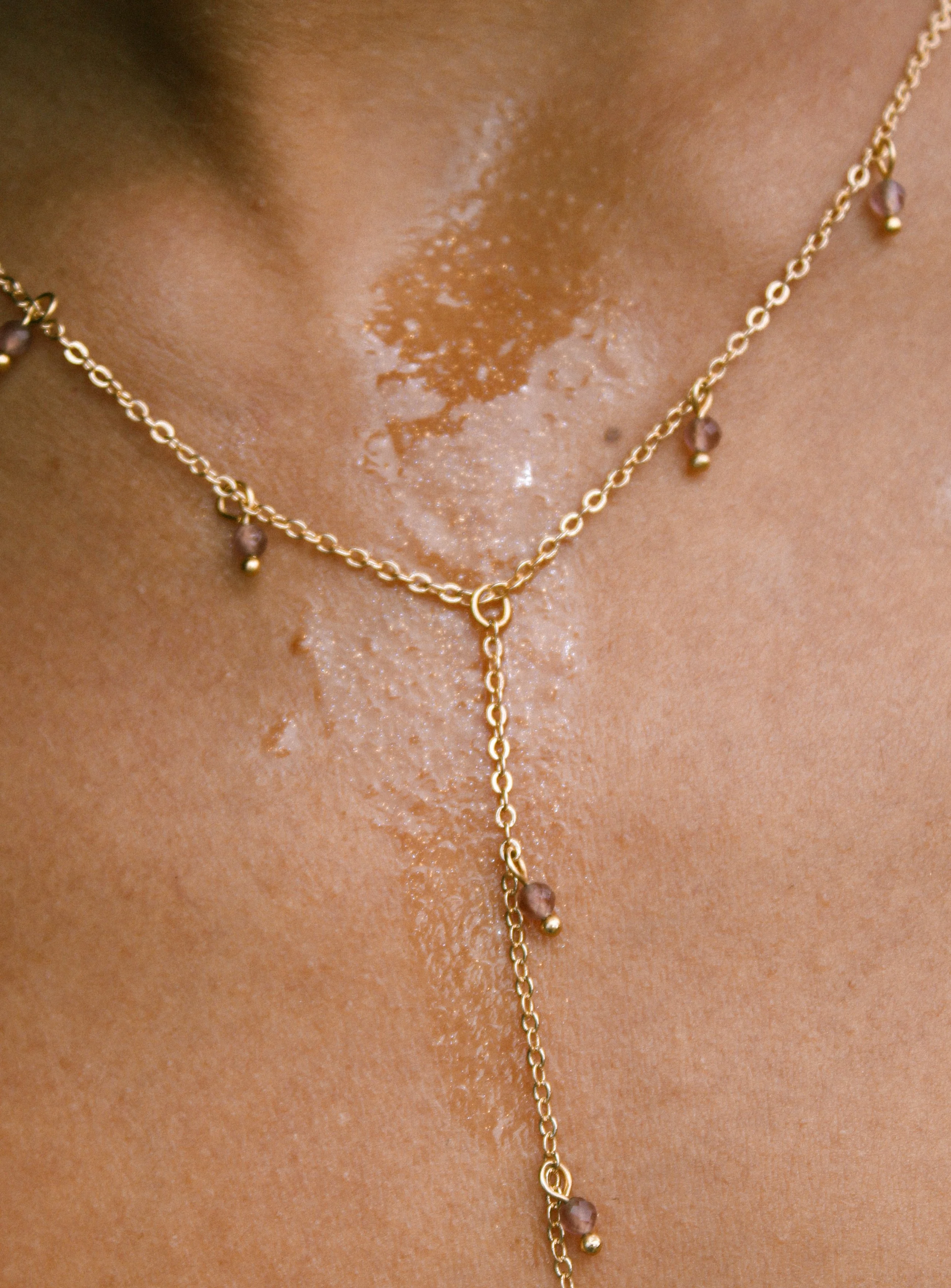 Close-up of a person's neck wearing a gold necklace with small purple beads.