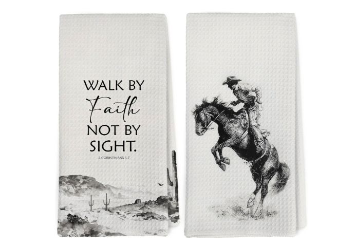 Two cloth hand towels with black and white designs. The left towel displays a quote: "WALK BY Faith NOT BY SIGHT" along with a desert scene and cacti. The right towel features a drawing of a cowboy riding a rearing horse.