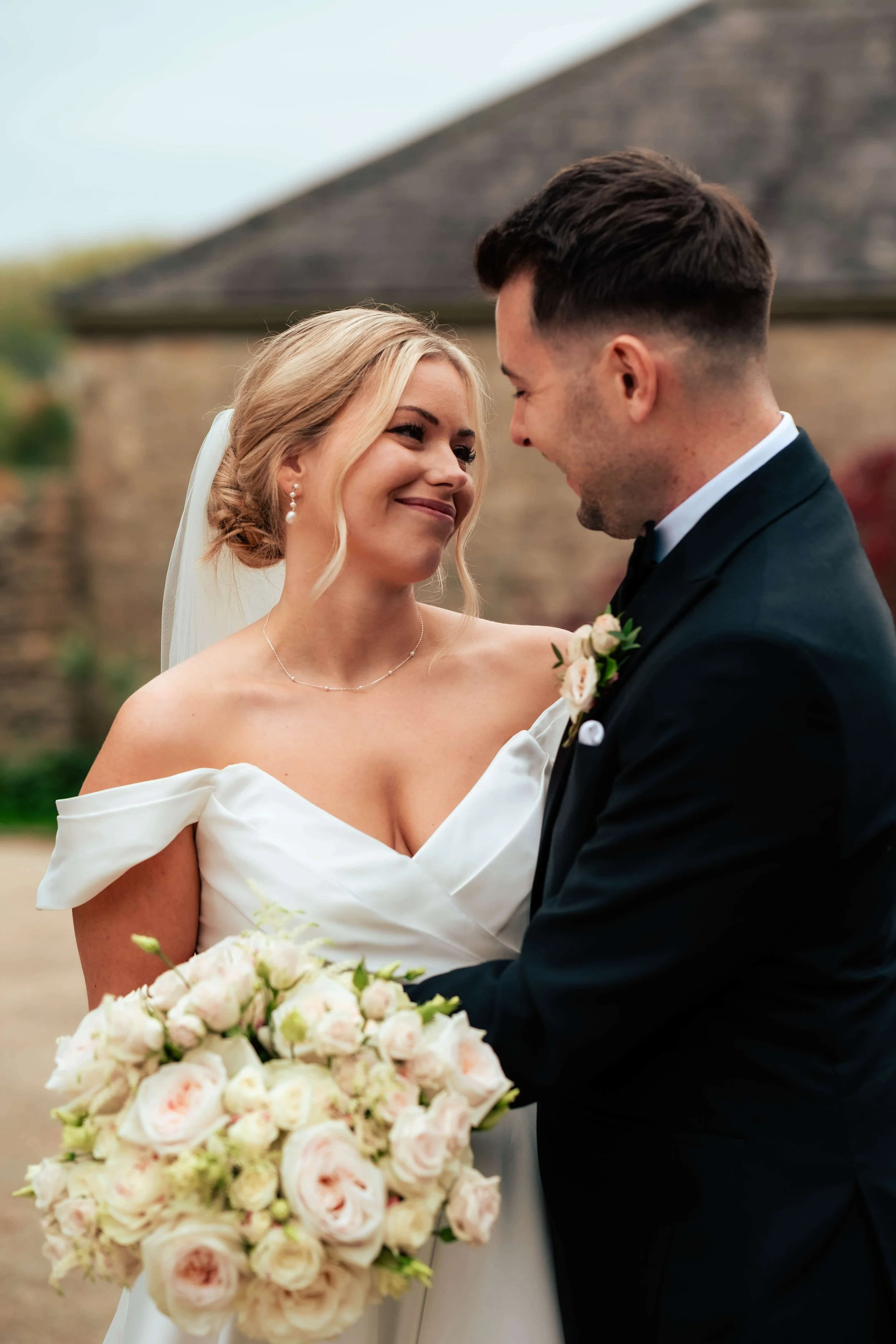 Bride and groom looking at each other while holding a bouquet of pink and white roses during their wedding ceremony outdoors.