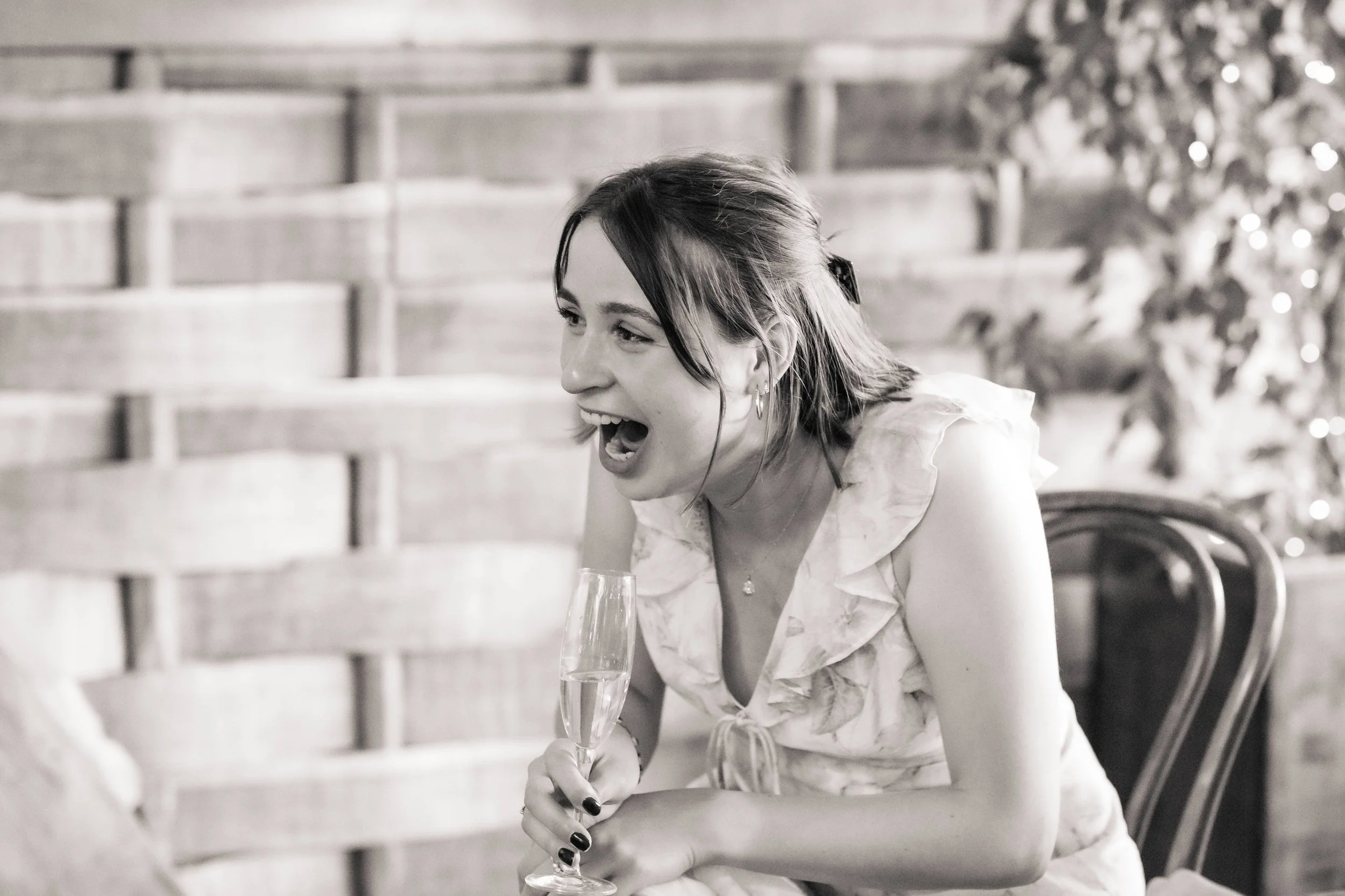 A woman smiling and laughing while holding a glass of champagne in a celebration setting.
