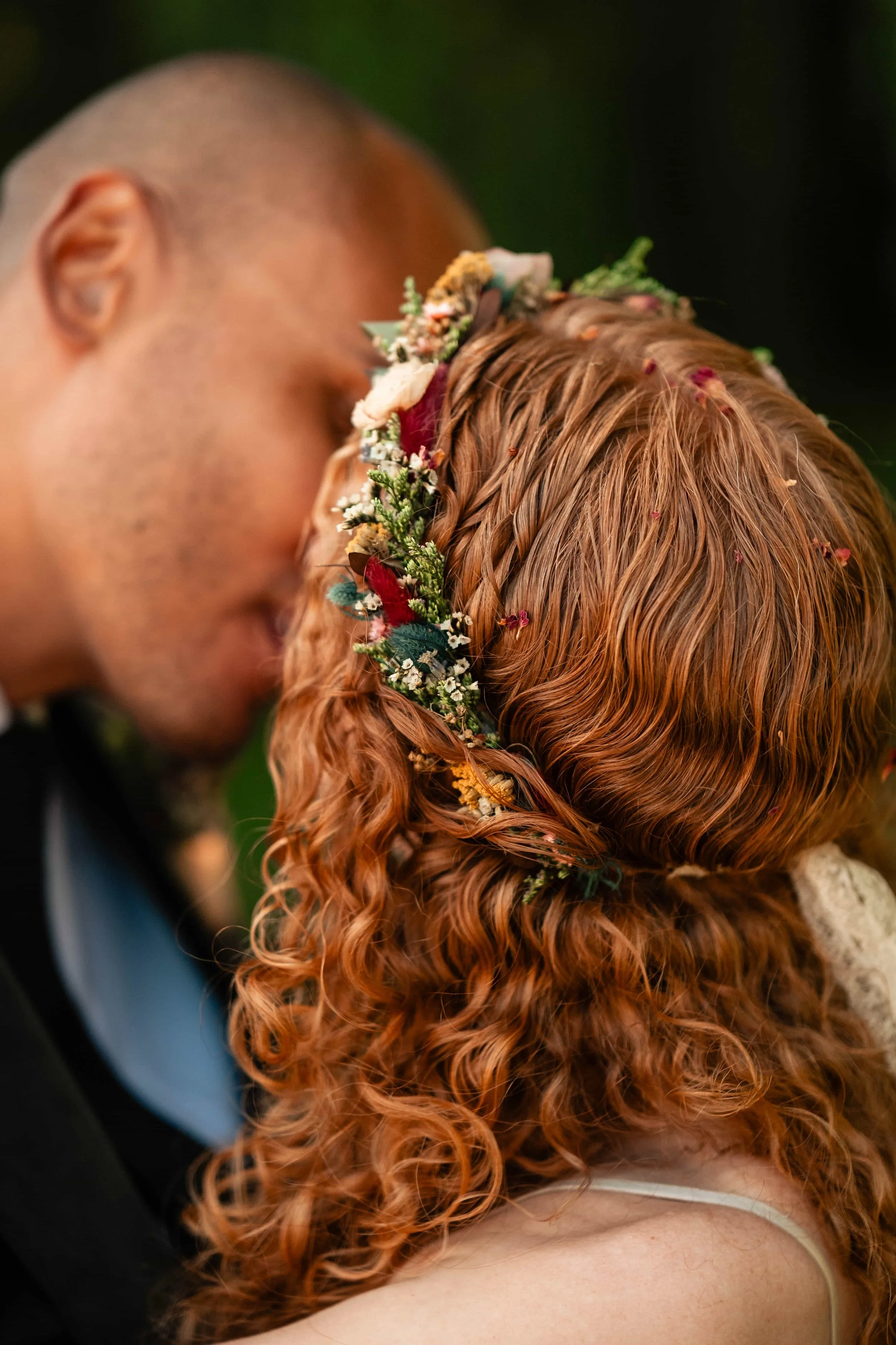 A couple with closed eyes sharing a tender moment, with the woman sporting red curly hair adorned with a floral crown.