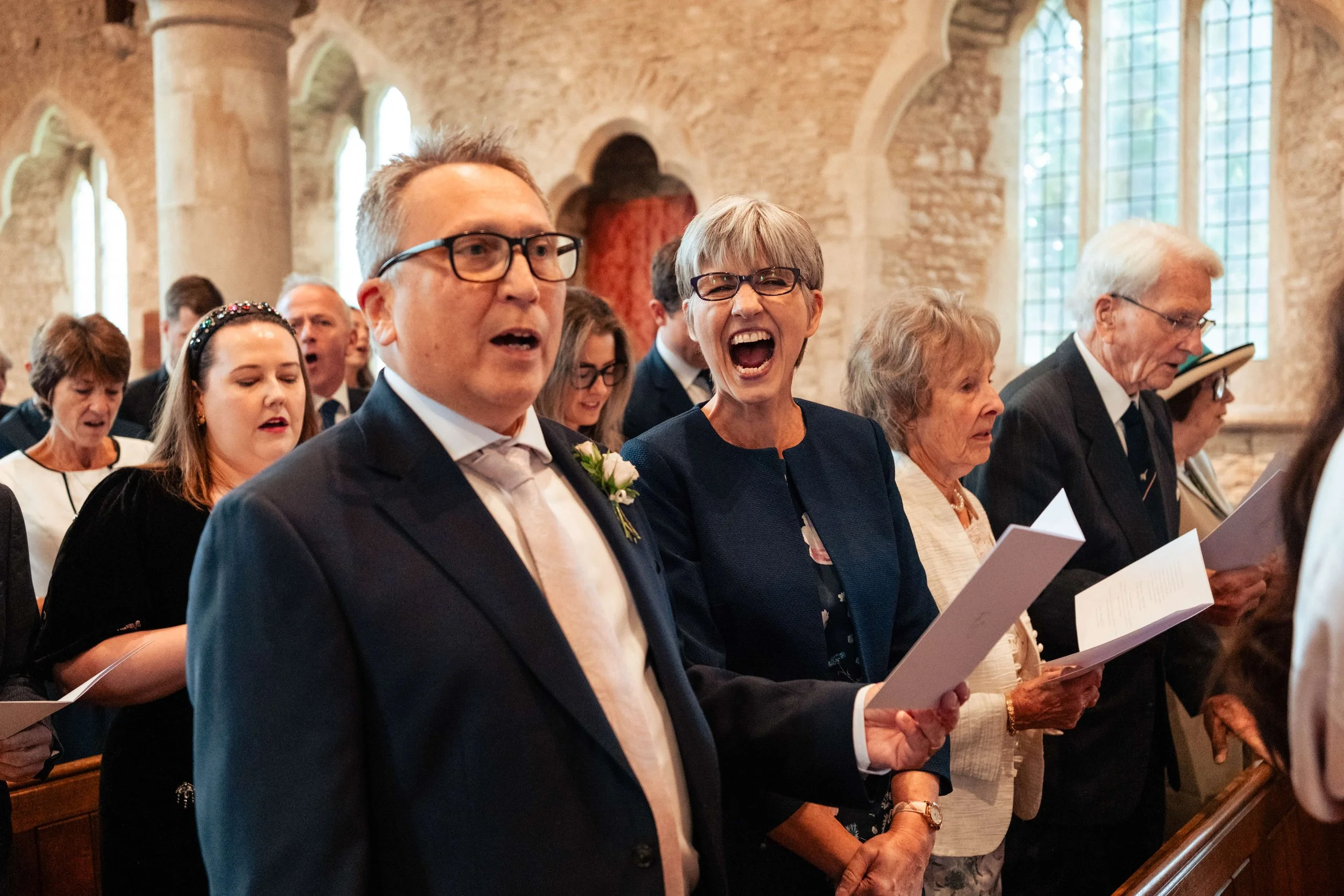 Group of people standing inside a church, singing from booklets, during a religious service.