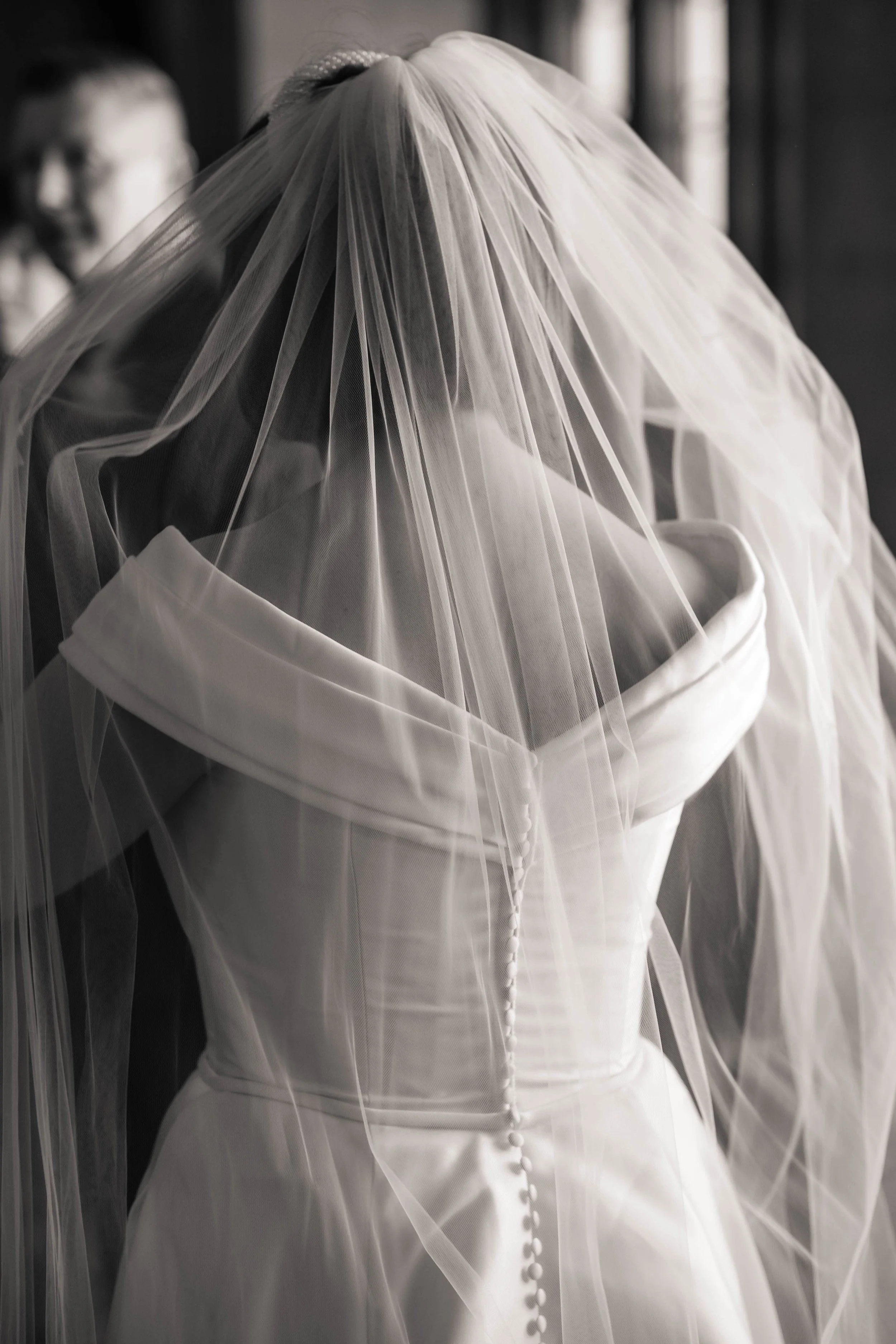 A wedding dress hanging with a veil draped over it, with a person in the background.