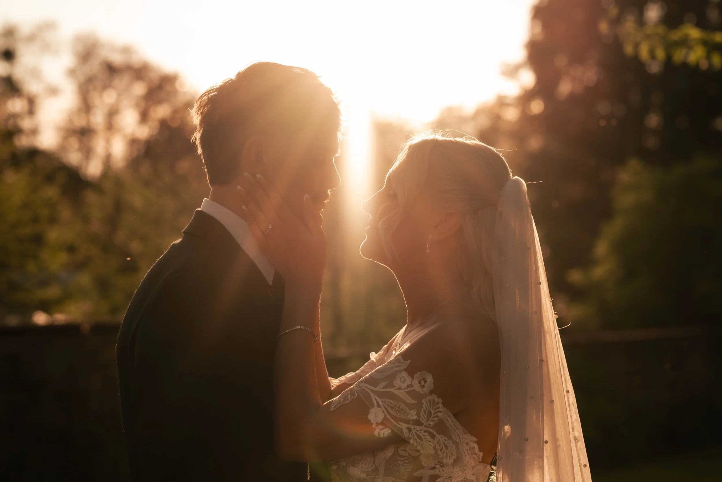 Bride and groom sharing an intimate moment in the sunlight, with the bride’s hand resting on the groom’s cheek.