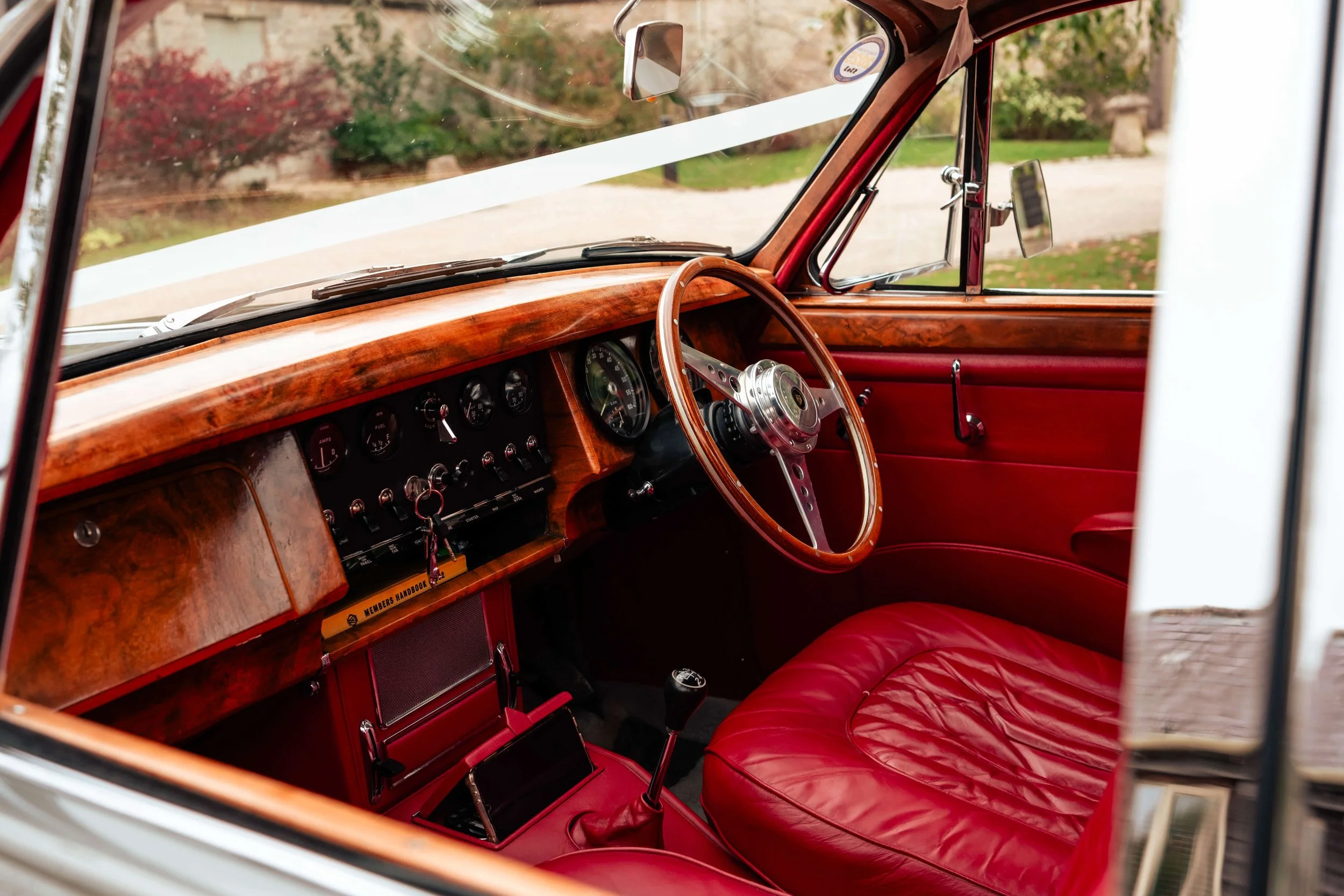 The interior of a vintage car featuring a wooden dashboard, red leather seats, a steering wheel, and various gauges and controls.