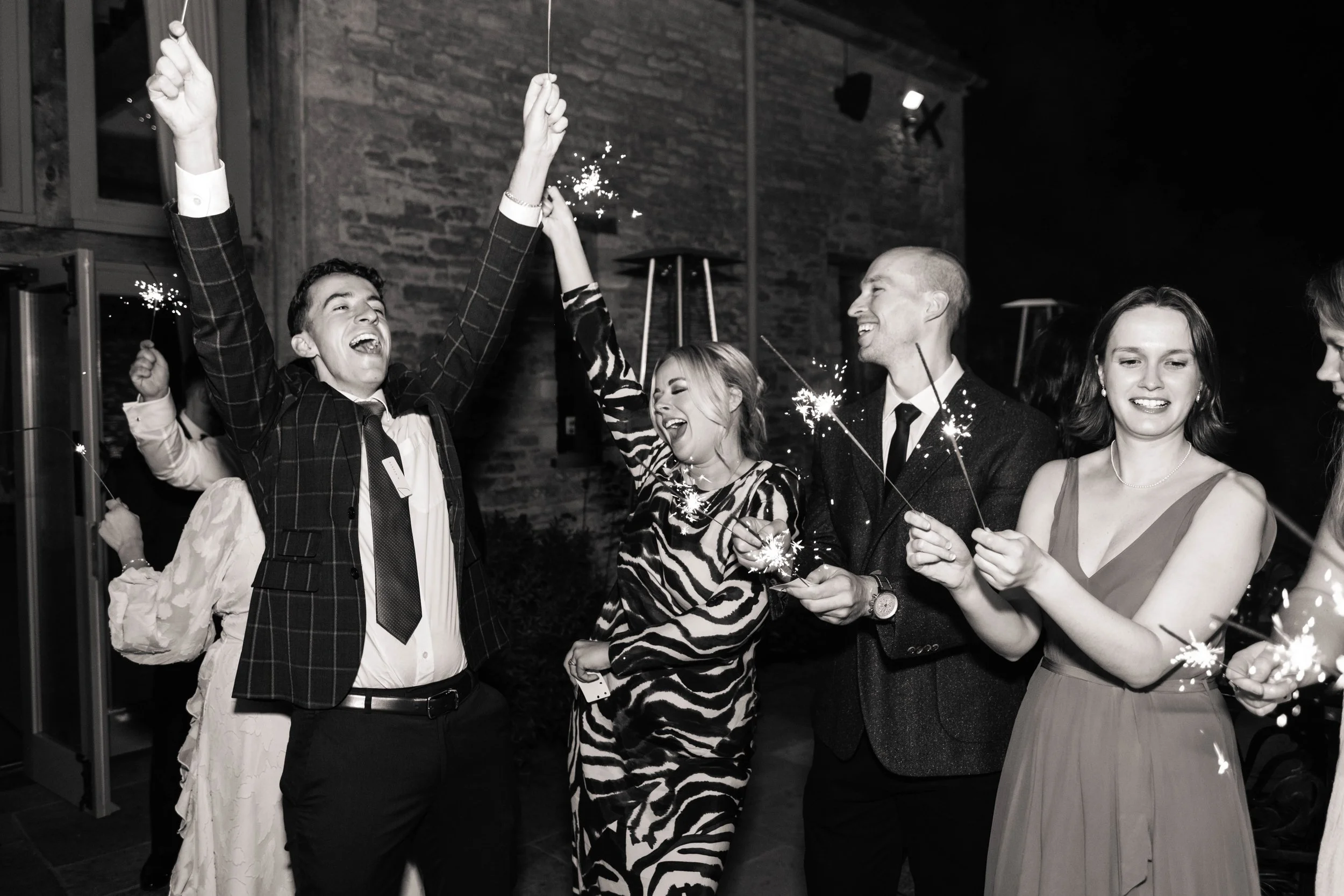 Group of people celebrating with sparklers at a party, smiling and dressed in formal attire, in a dimly lit indoor setting.