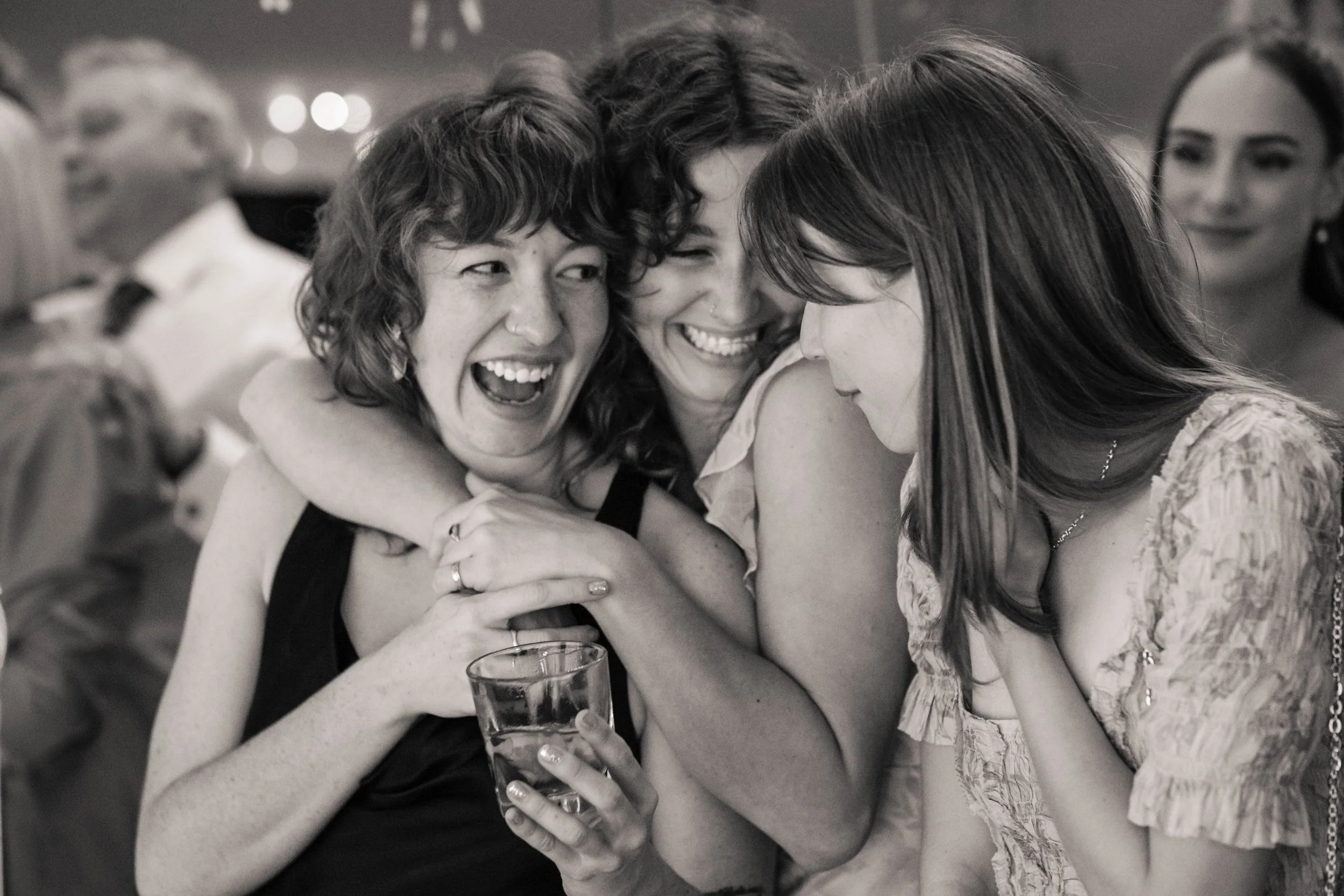 Three female wedding guests hugging and celebrating together on the wedding reception dance floor.