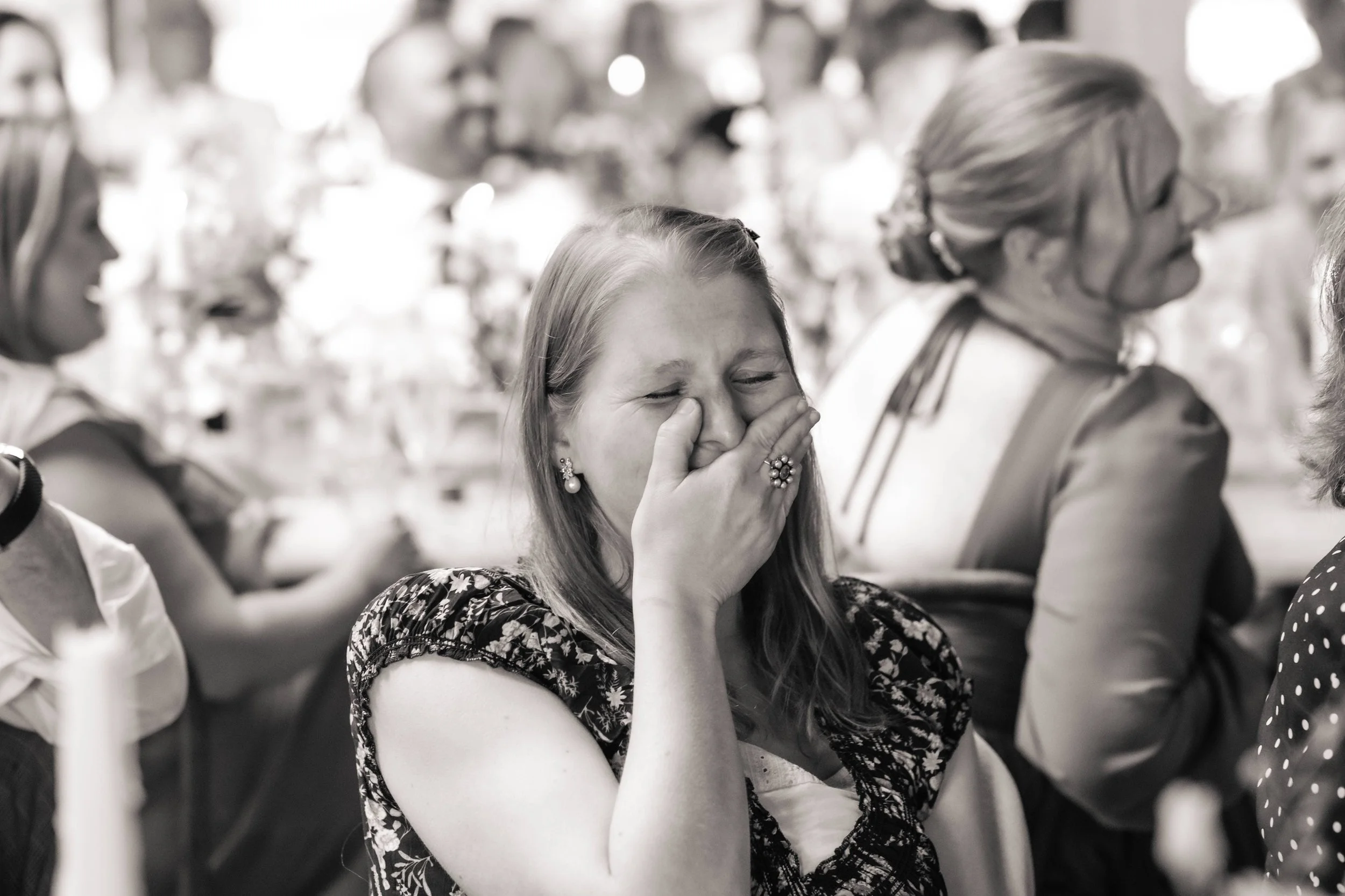A young woman with earrings and a ring on her finger is crying and covering her mouth with her hand, surrounded by other women in a gathering or celebration.