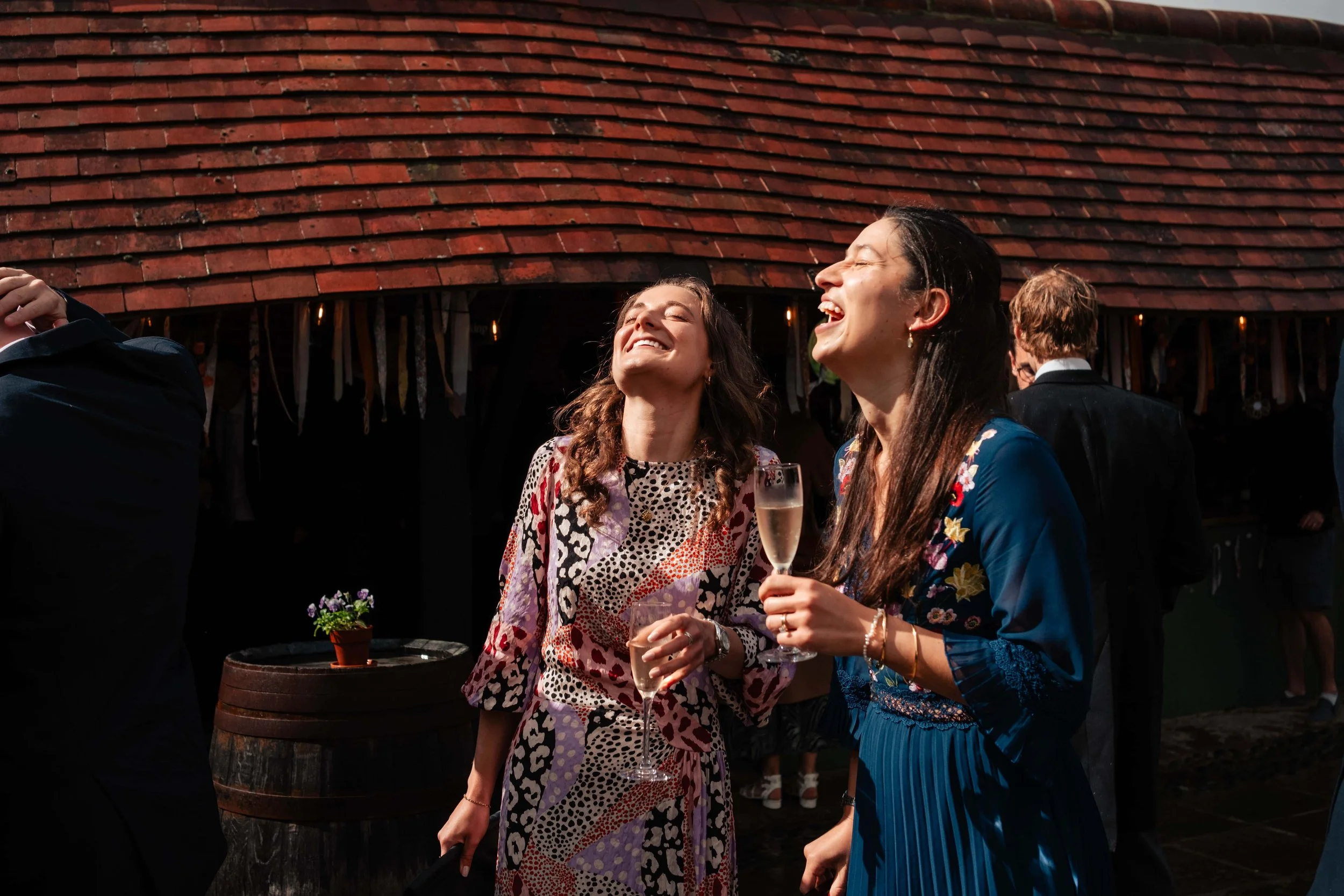 Two women sharing a laugh while holding champagne glasses at an outdoor social gathering.