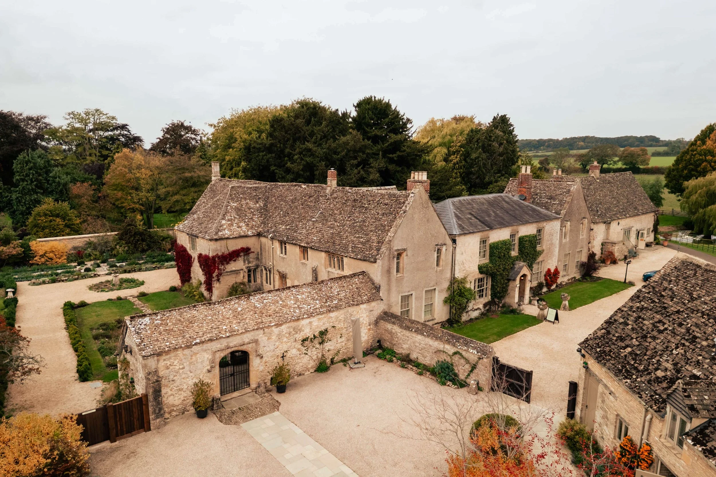 Aerial view of Caswell House wedding venue in Oxfordshire, a historic stone manor with a courtyard surrounded by trees and gardens.