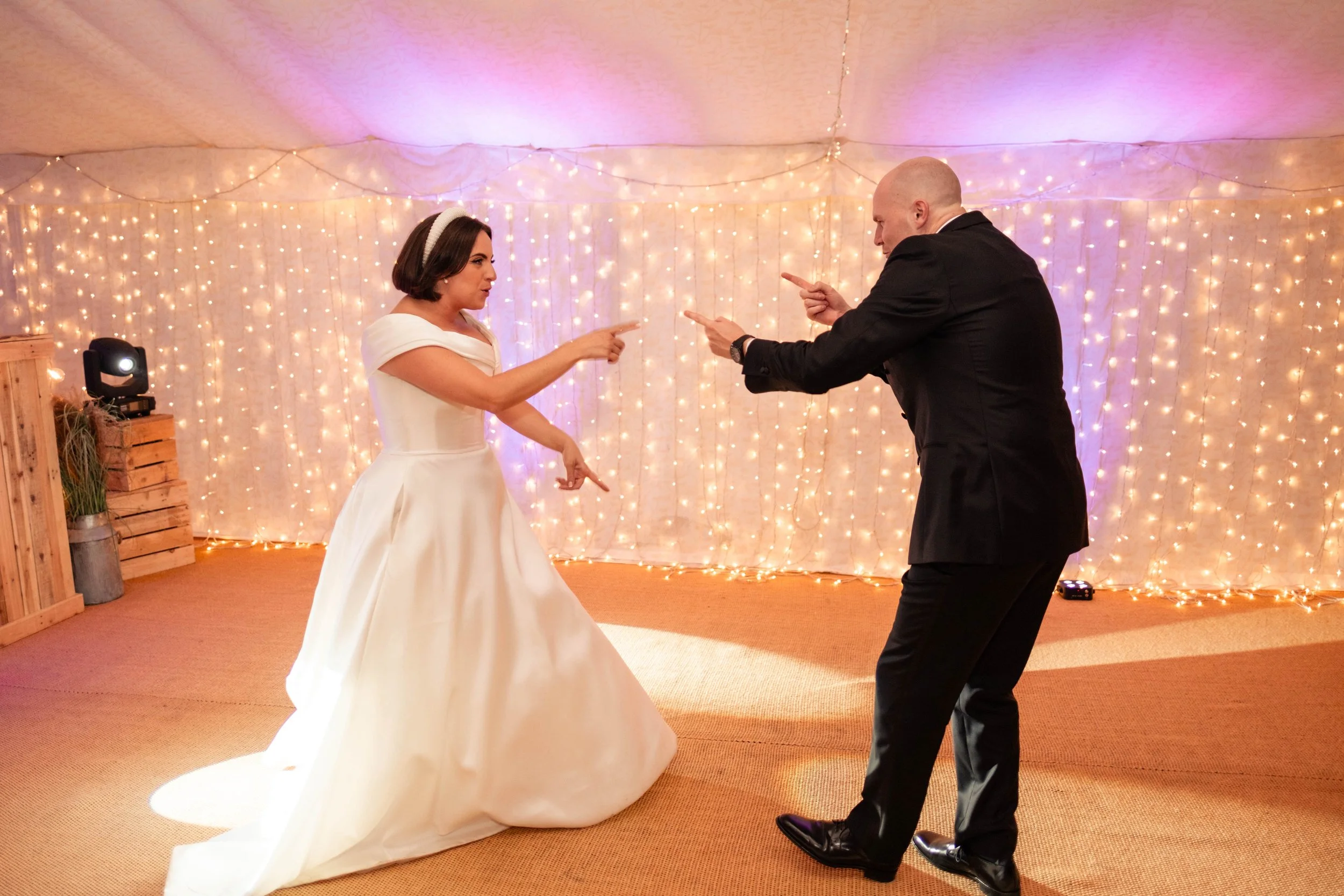 A bride and a man are dancing together at a wedding reception with fairy lights in the background.