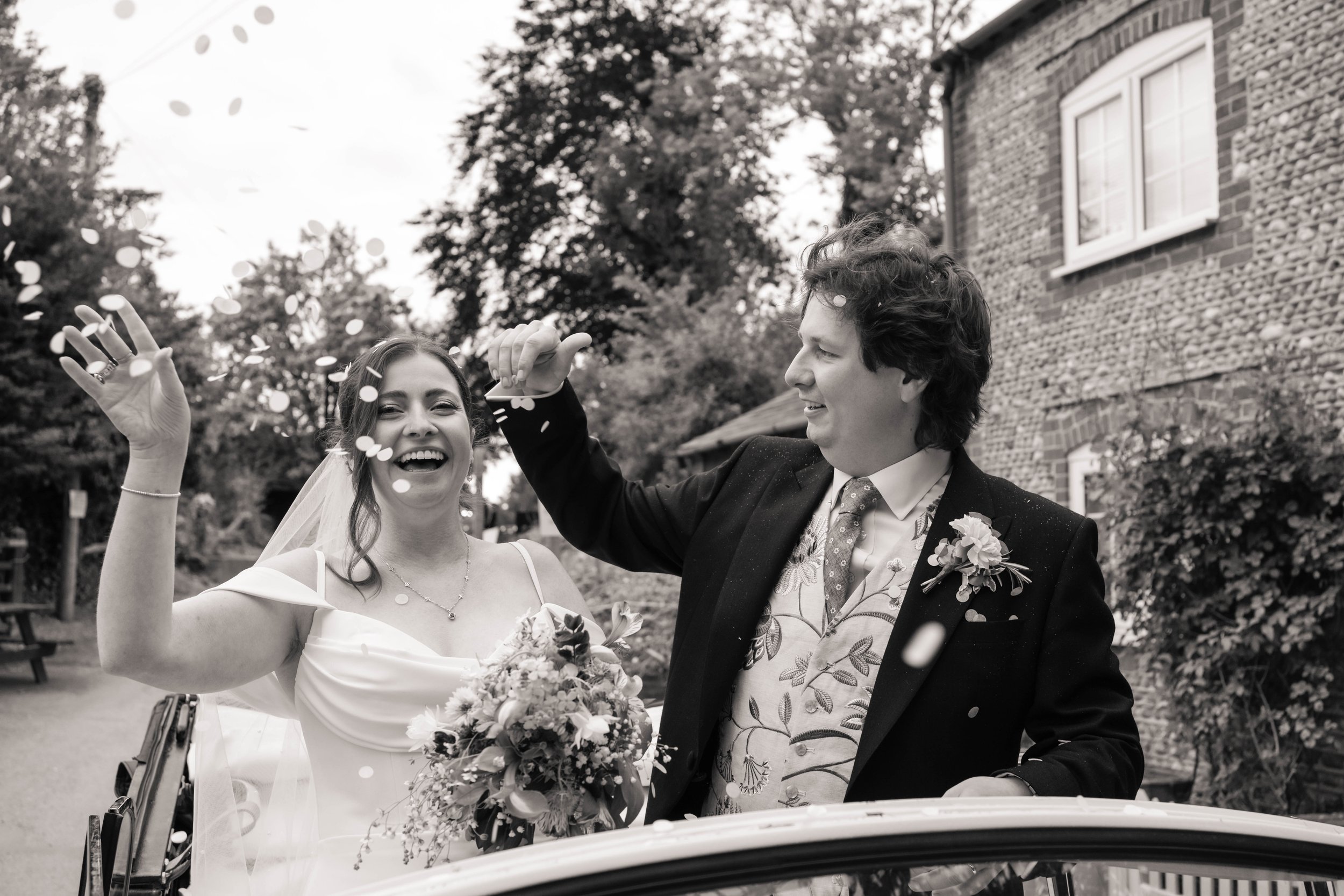 Bride and groom standing in their car throwing confetti around them after their wedding ceremony.