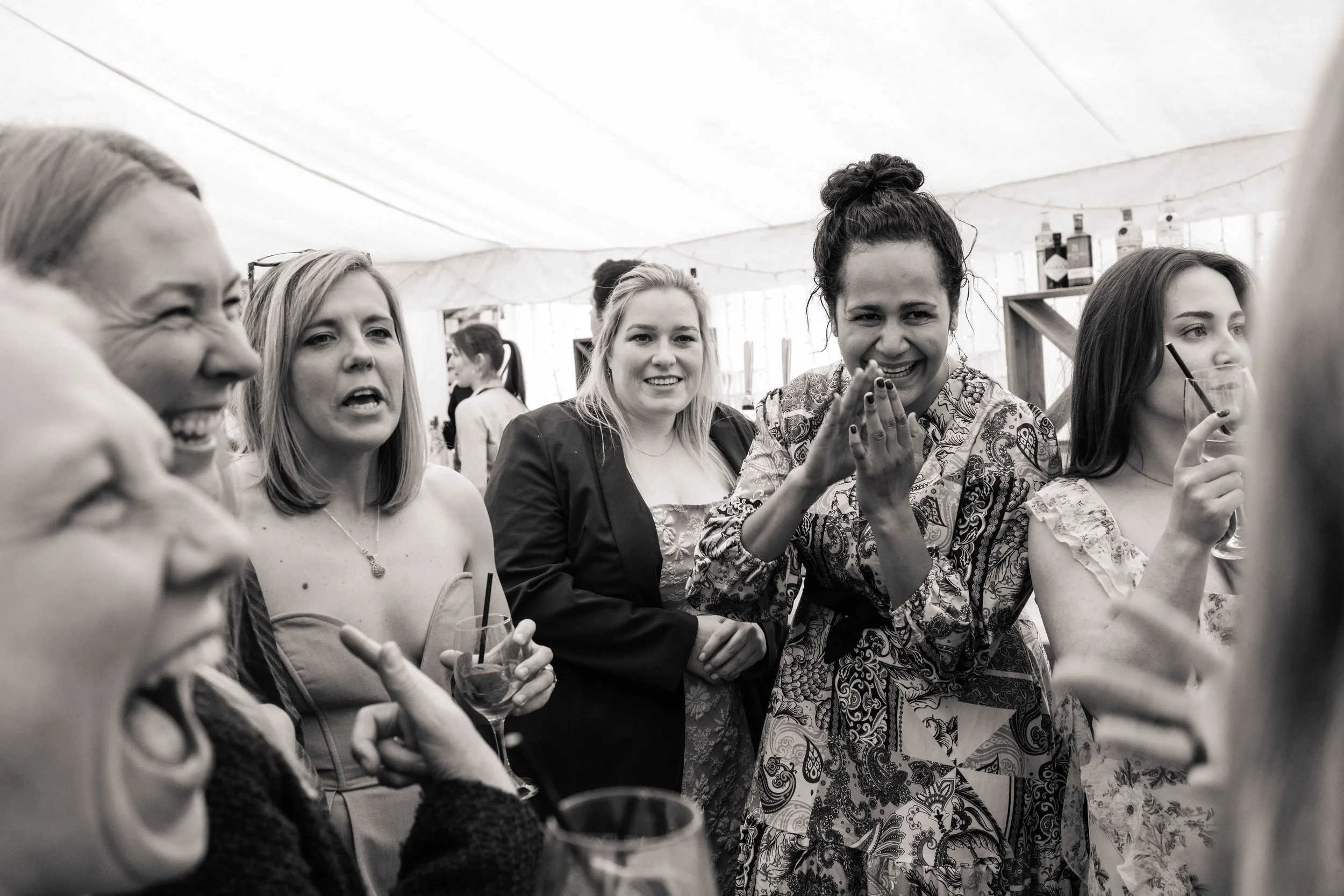 Women wedding guests laughing together at a reception in a marquee at The Perch in Oxford.