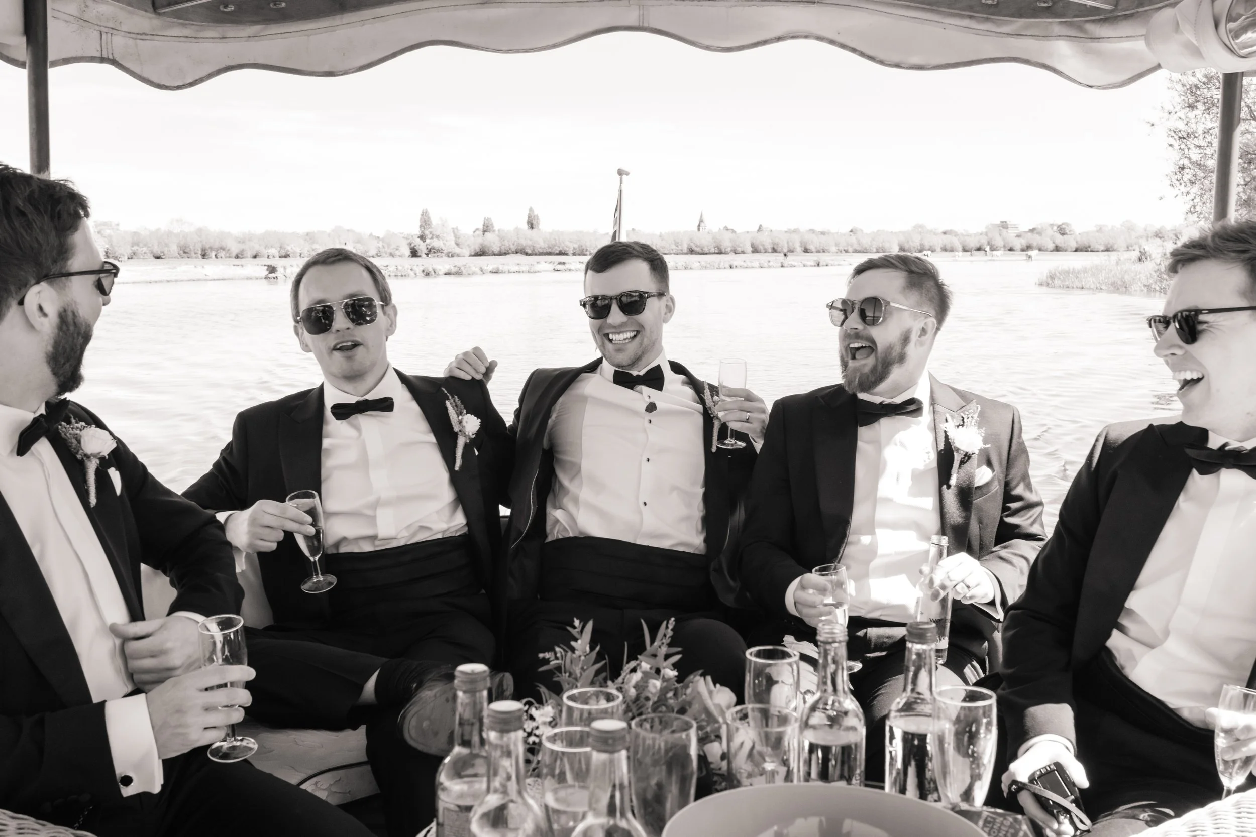Groomsmen laughing together on a river boat during the wedding.