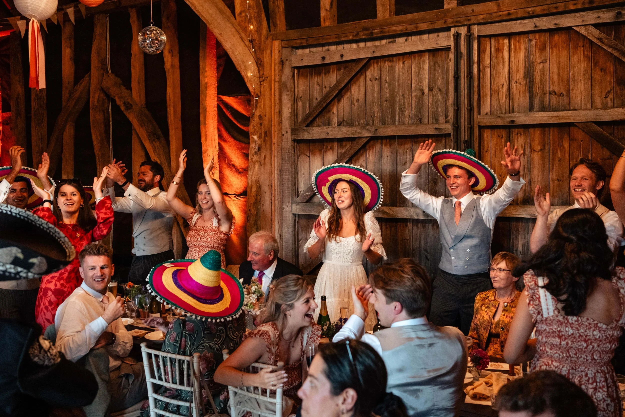 People celebrating at a festive event wearing colorful sombreros, dancing, and enjoying a lively atmosphere in a rustic wooden venue.